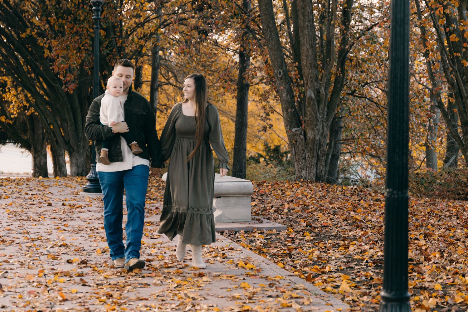 People walk together on a path covered in golden autumn leaves.