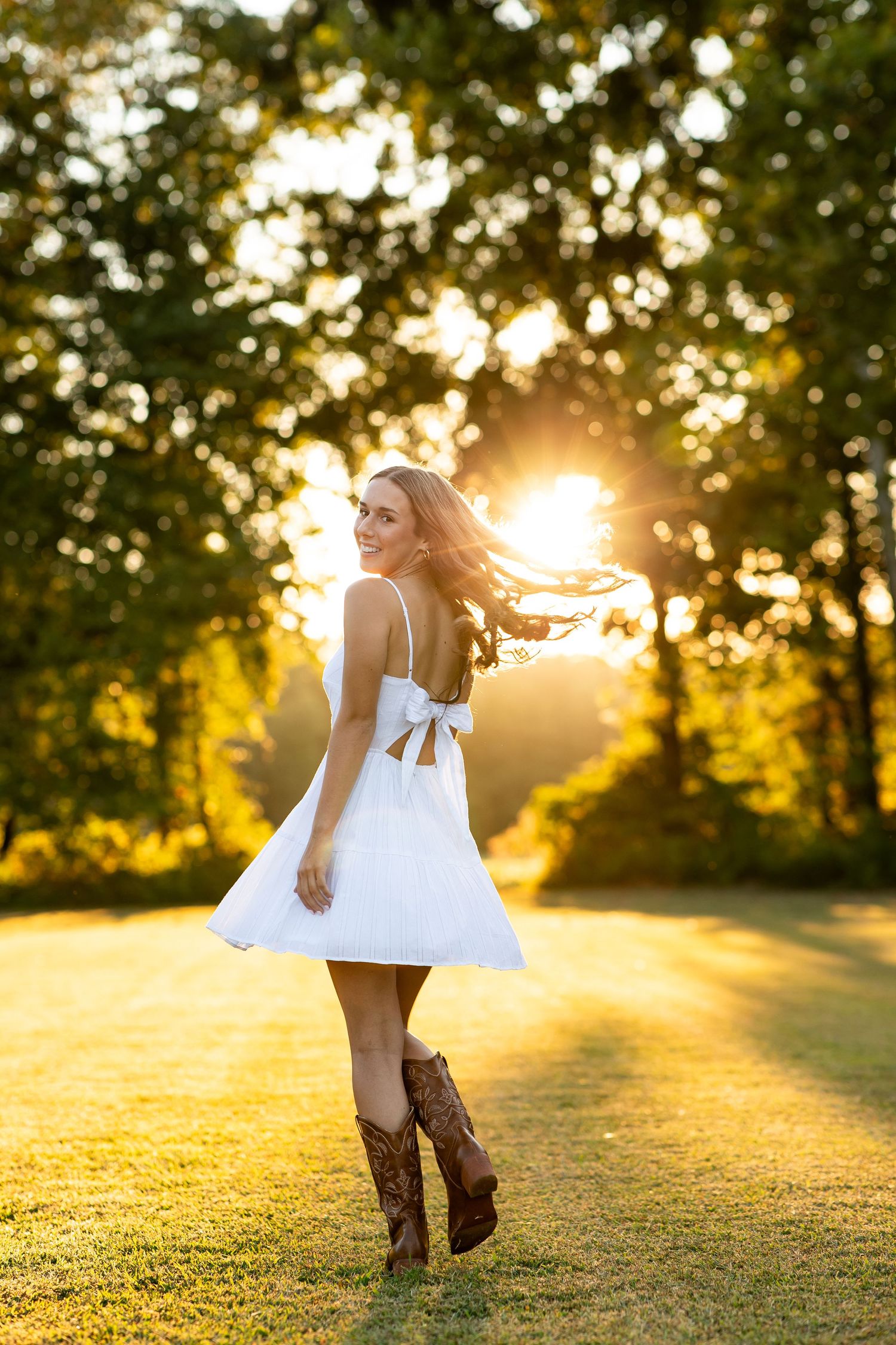 A white dress twirls in golden sunlight on grassy hill during sunset creating a dreamy summer scene.
