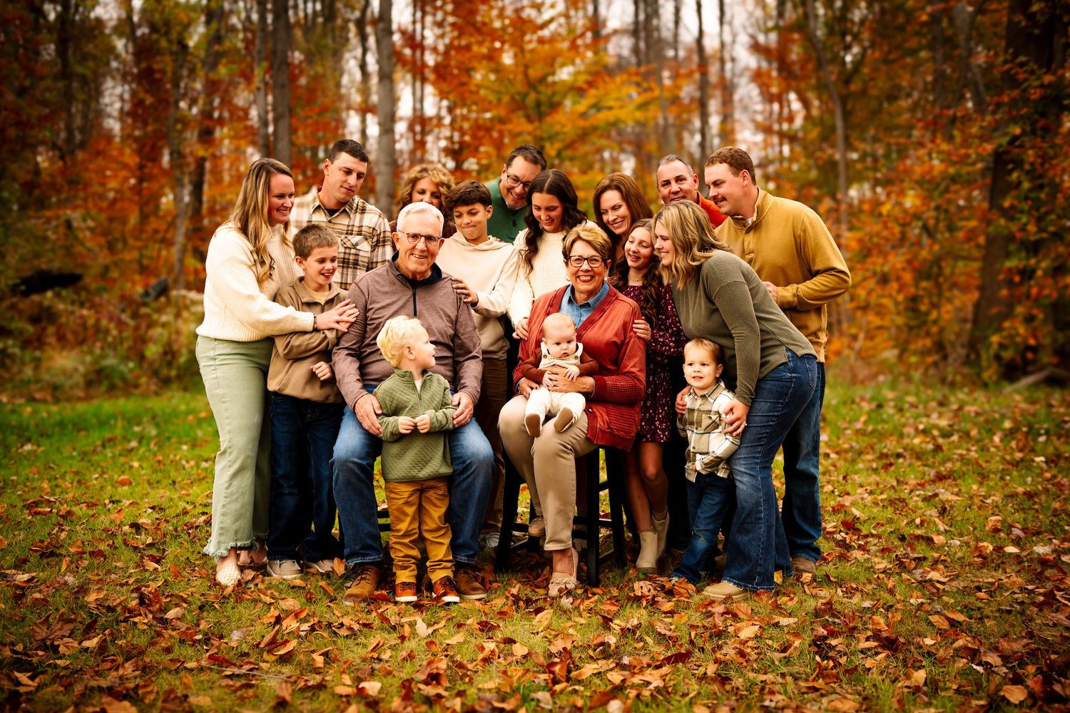 A large group poses together outdoors during autumn with colorful fall foliage in the background.