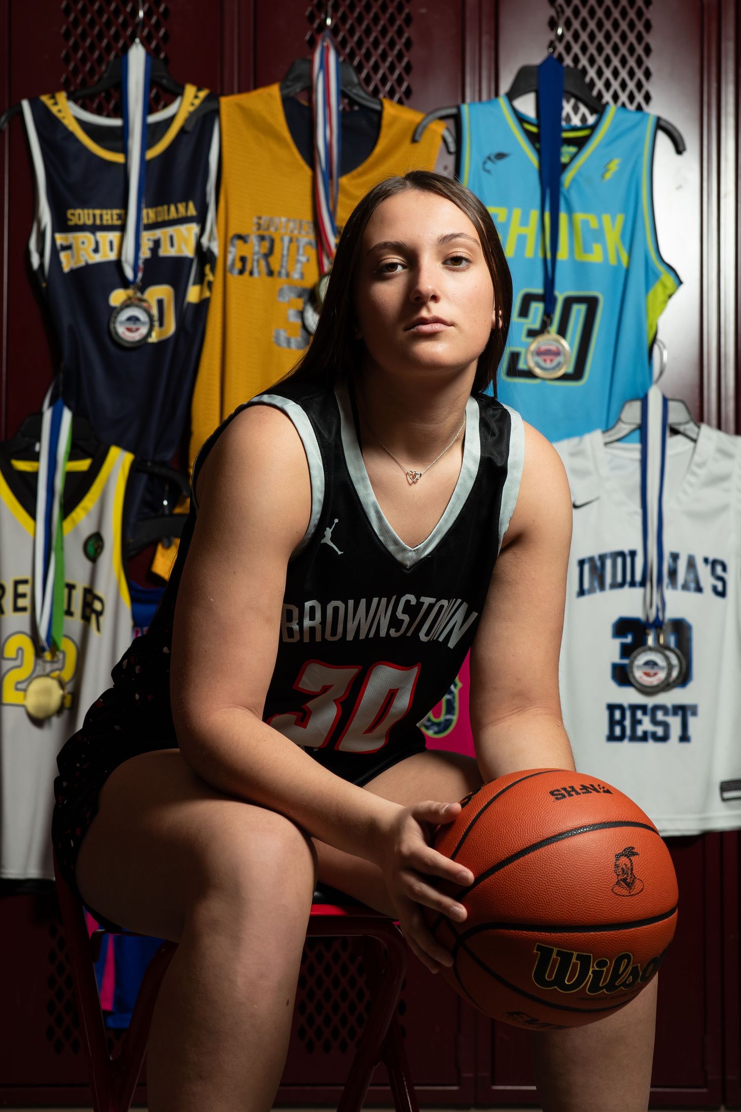 Basketball player poses in front of jersey display case holding ball in dramatic lighting sequence.