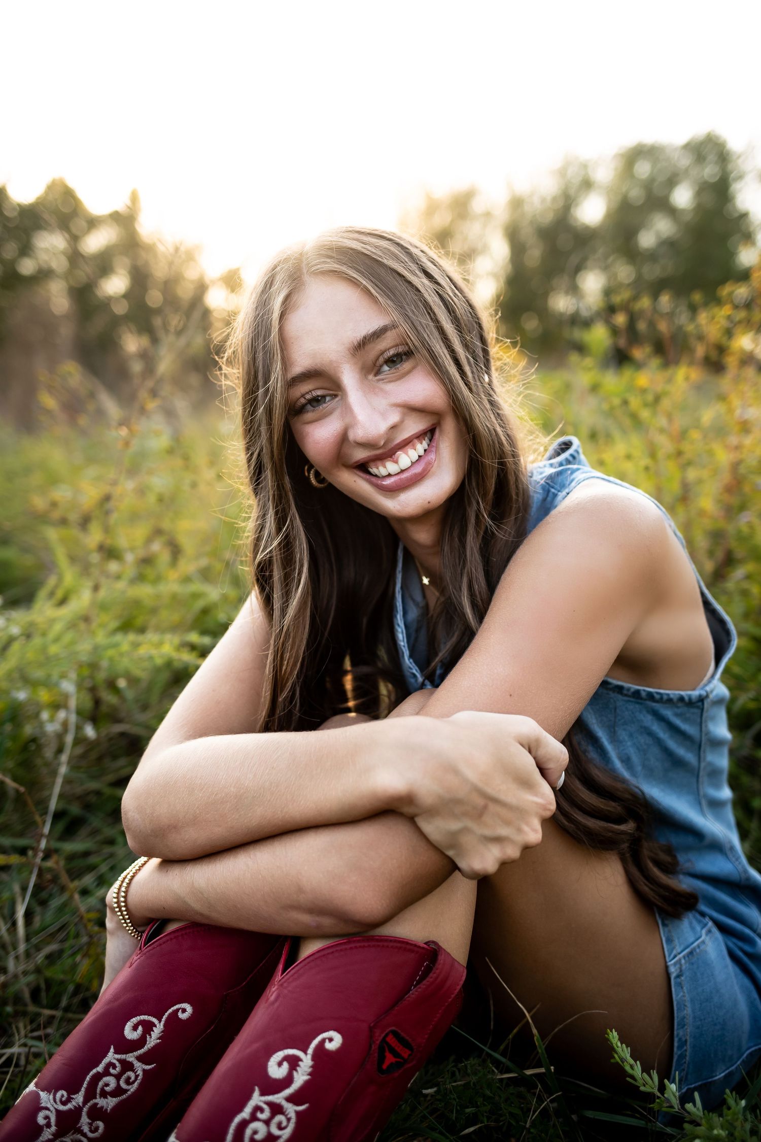 A series of outdoor portrait photos showing someone in denim and burgundy clothing sitting in a sunlit field with wildflowers.