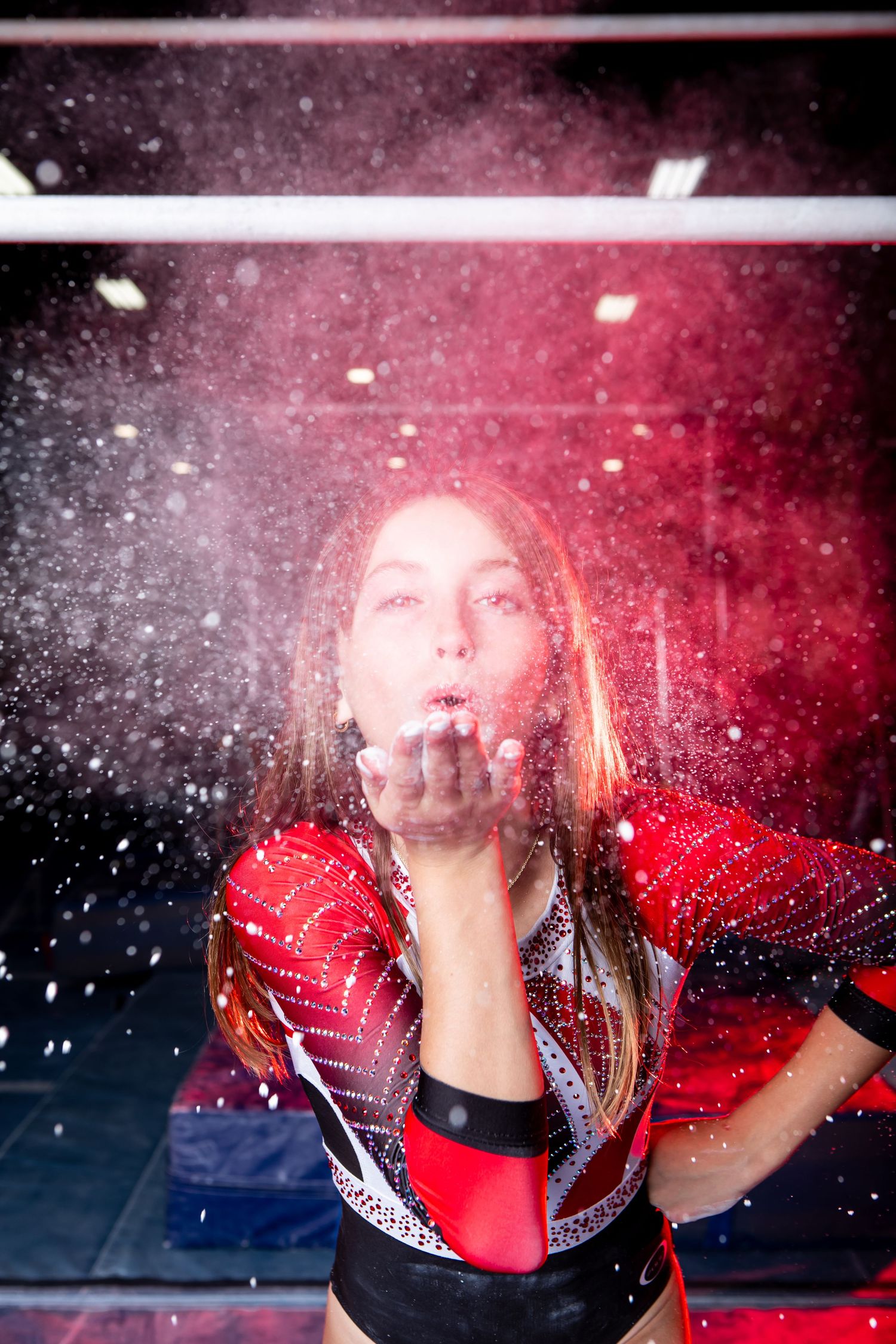 A person blows chalk creating a dramatic spray of chalk against a red and black background.