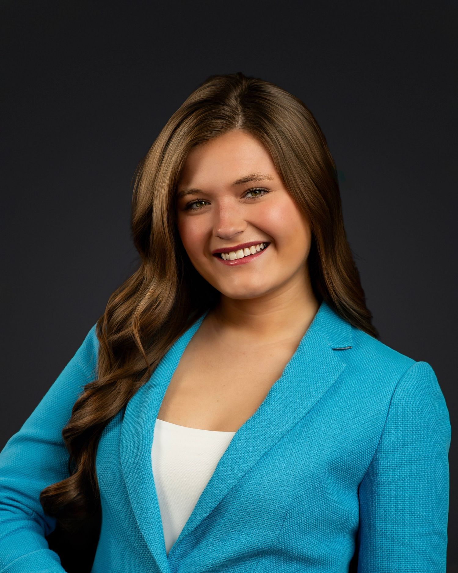 Professional headshot portrait of someone in a bright turquoise blazer and white top against a dark background.