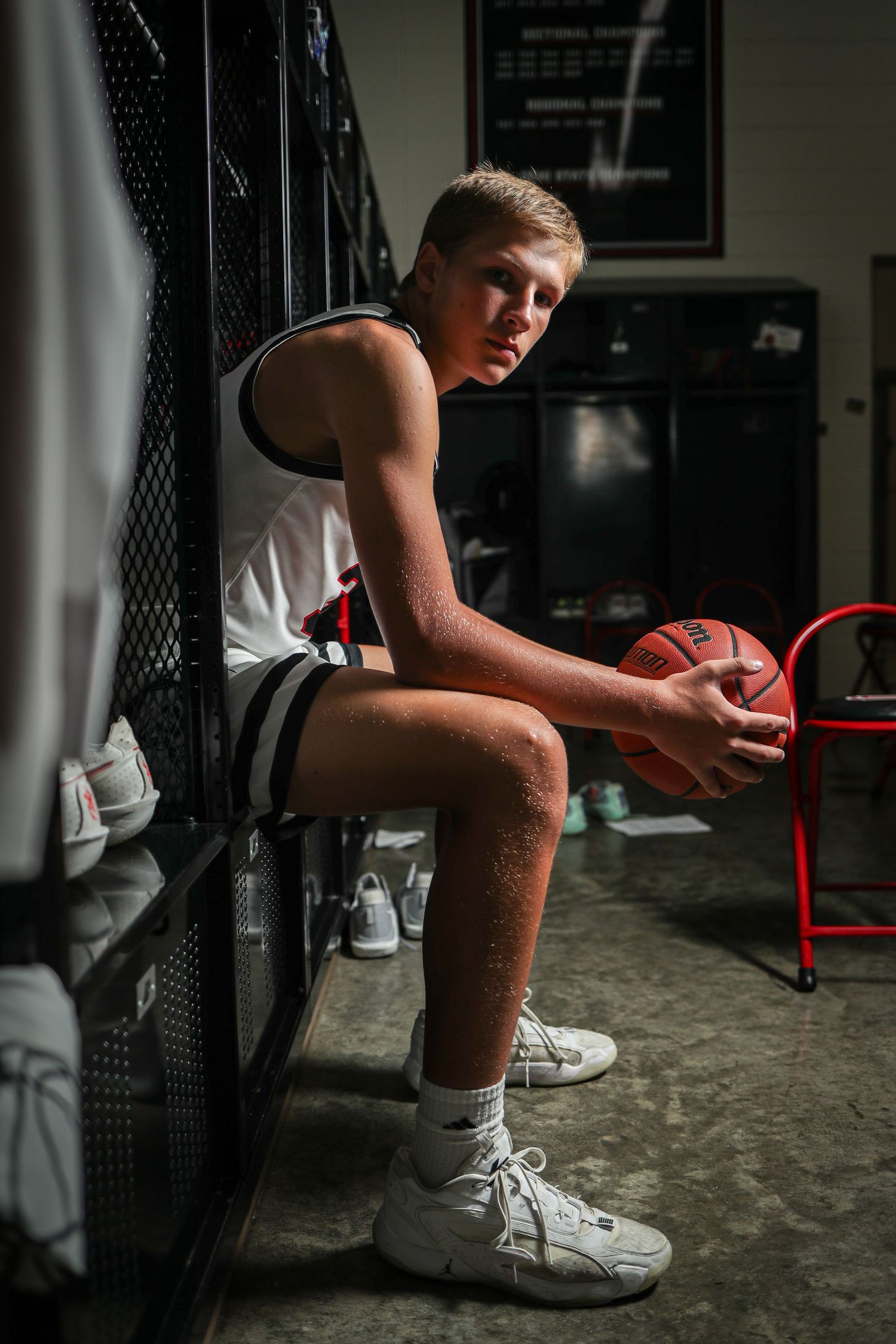 Basketball player in white shoes sits on bench  in dark gym setting.