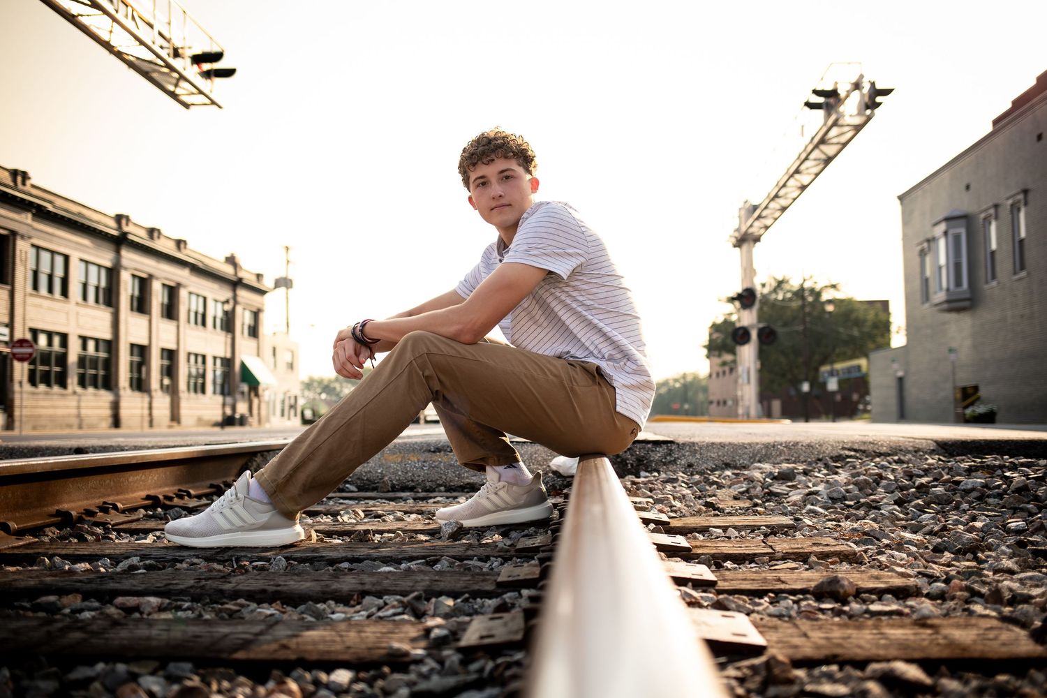 A person in white sits on train tracks during golden hour with urban buildings in the background.