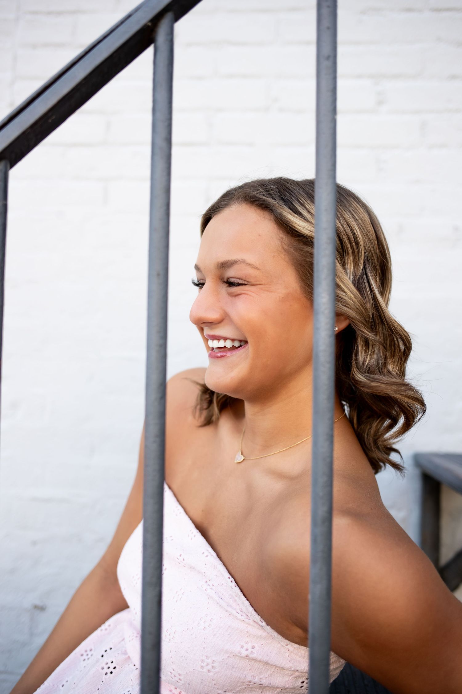 Smiling person in pink top looking through metal bars with a playful expression.