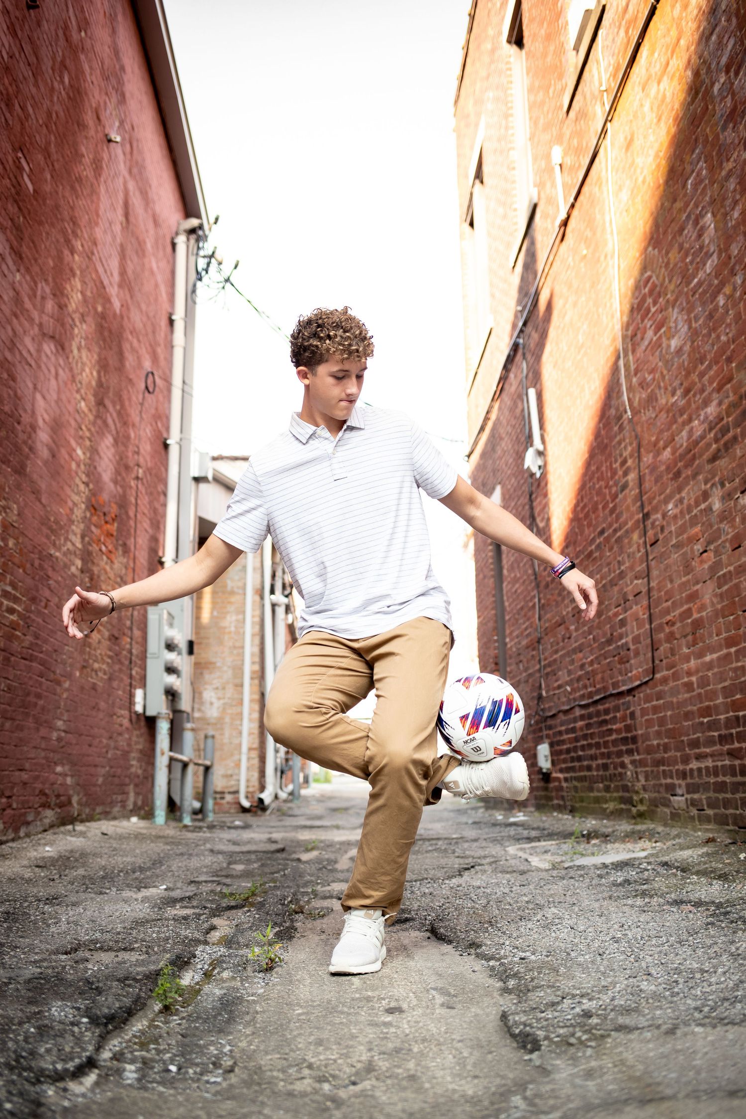 A person in khaki pants and white shoes performs a jumping sequence in an urban alley with brick walls.