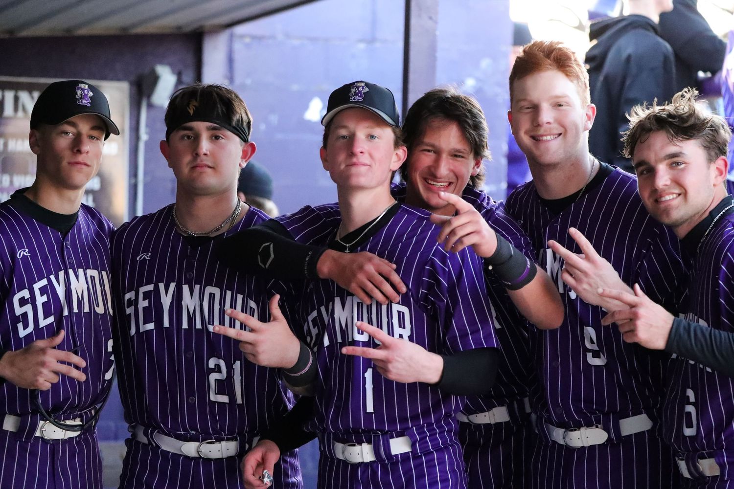 Baseball team players in purple pinstriped uniforms pose together in dugout showing team spirit and camaraderie.