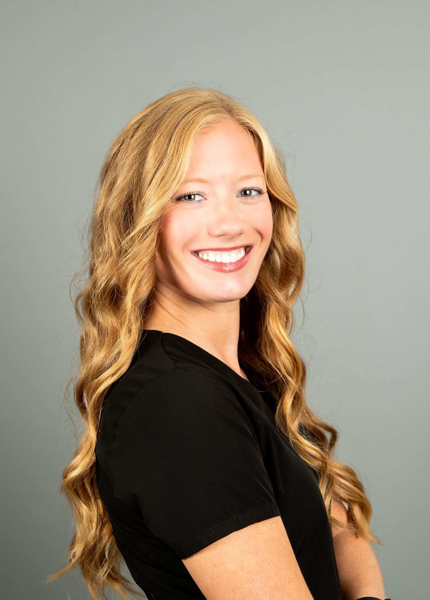 A person with wavy blonde hair wearing a black top poses in a series of headshots against a gray studio backdrop.