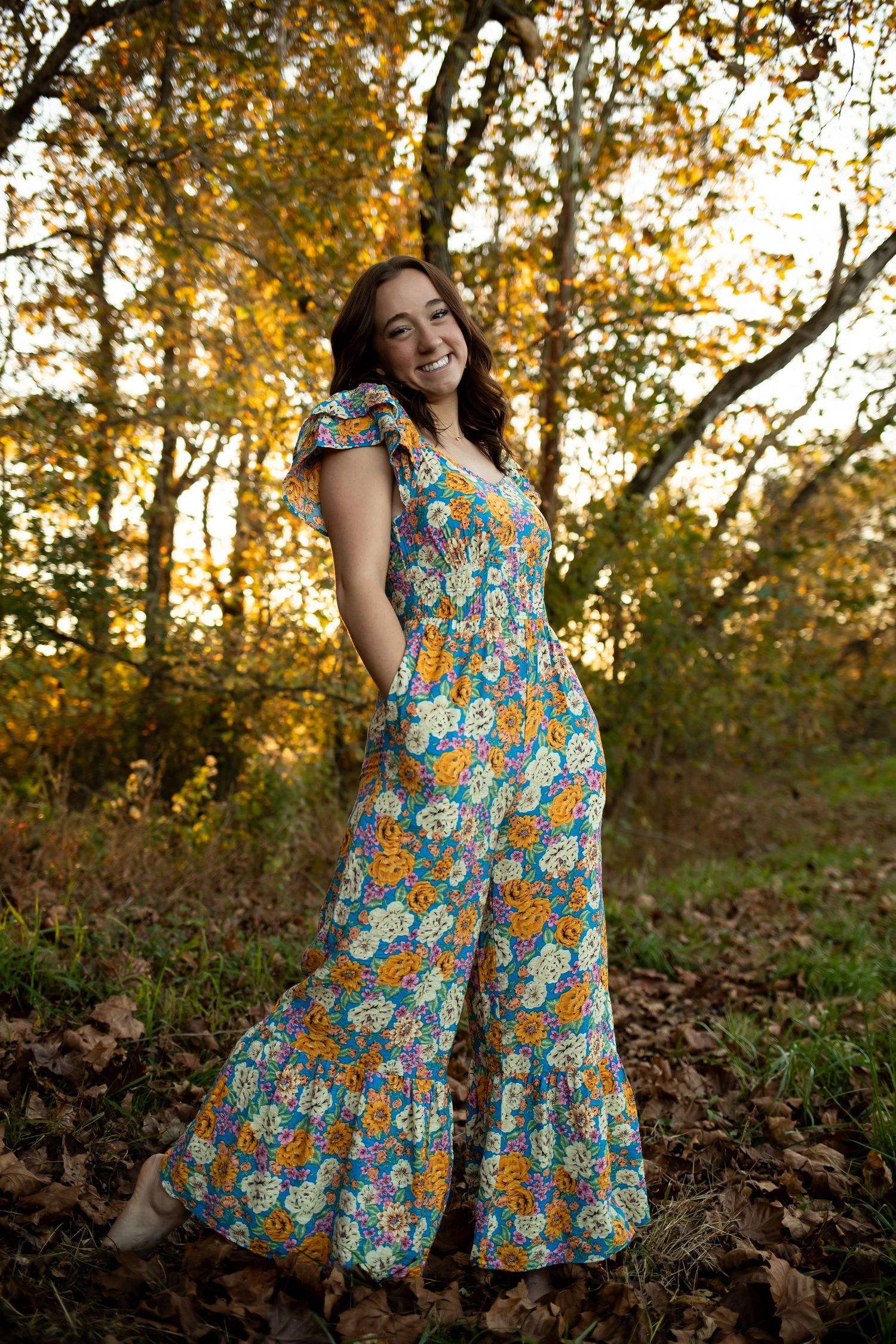 Someone wearing a colorful floral dress twirls playfully in an autumn forest setting during golden hour.