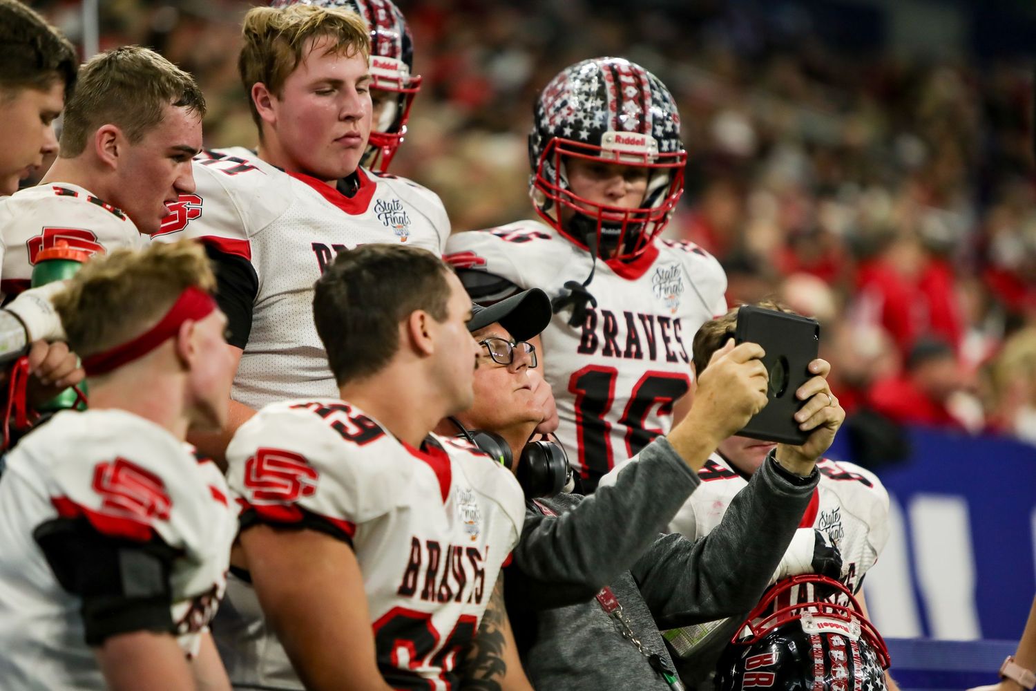 Football players in red and white uniforms huddle together on the sidelines during a game.