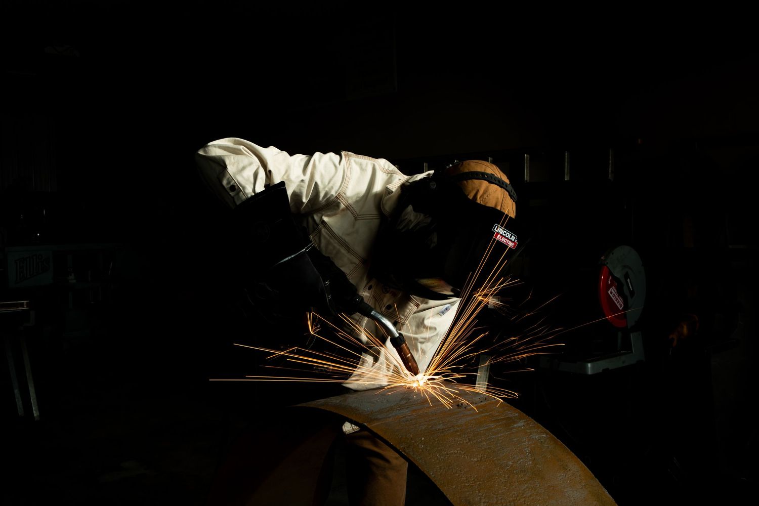A welder creates bright sparks while working on metal in a dark industrial workshop.