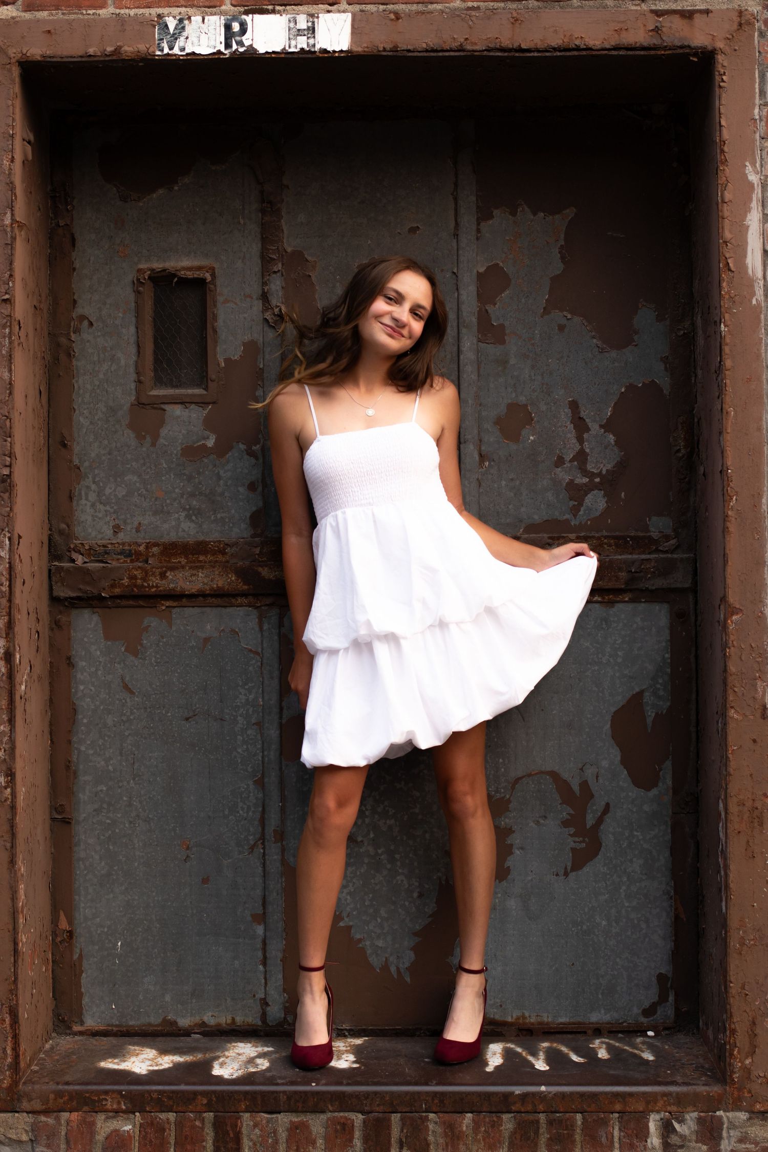 A person in a white dress poses creatively in industrial metal storage cubbies or compartments.