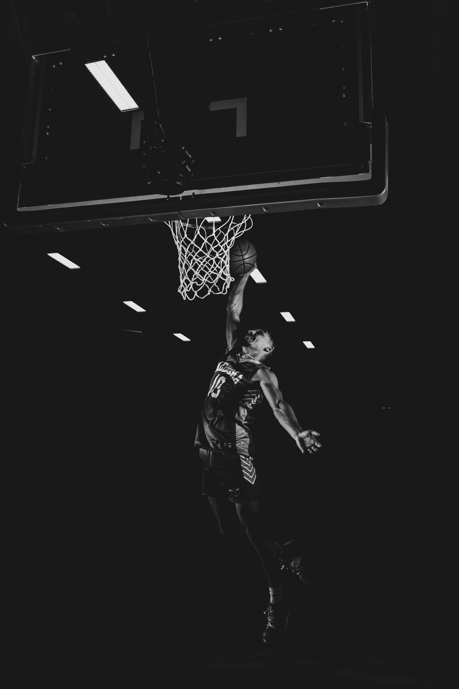 A basketball player soars high above the court for a slam dunk in dramatic black and white lighting.