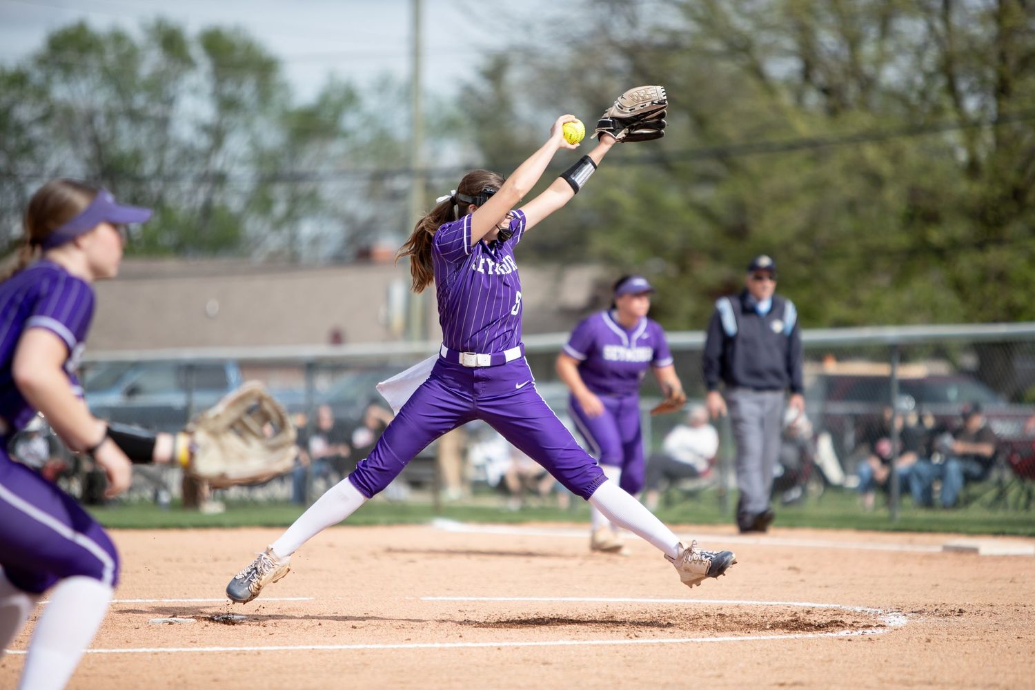A softball player in purple uniform slides into base during an intense game moment on the dirt infield.