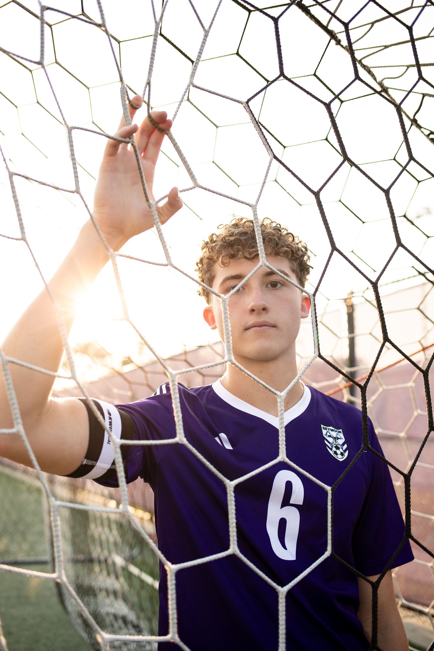 Athletes in purple jerseys pose behind a sports net during sunset.