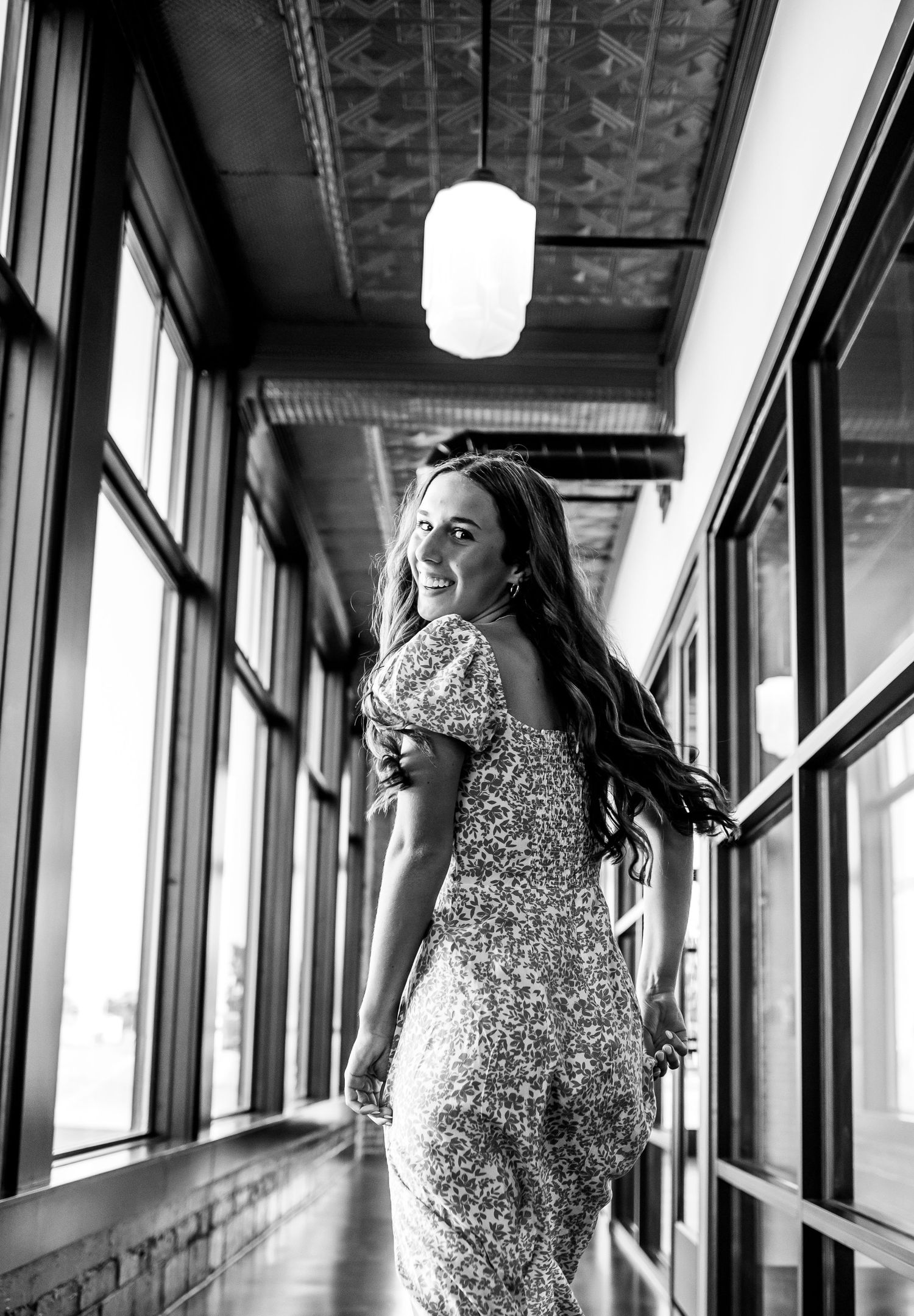 Black and white portrait of someone in a sequined dress posing playfully in a sunlit hallway.