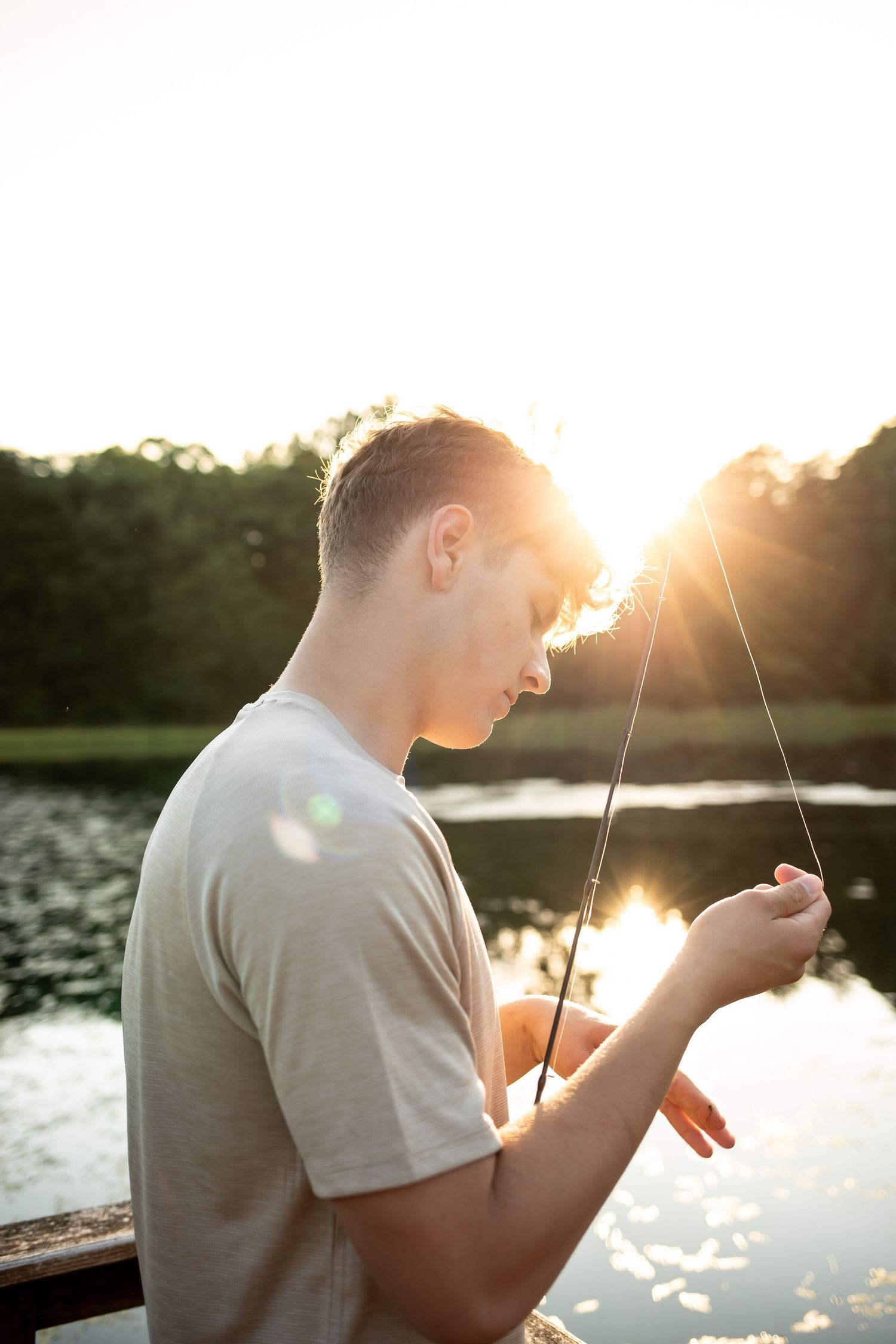 Person fishing on a lake at sunset with golden sunlight creating a warm silhouette effect.