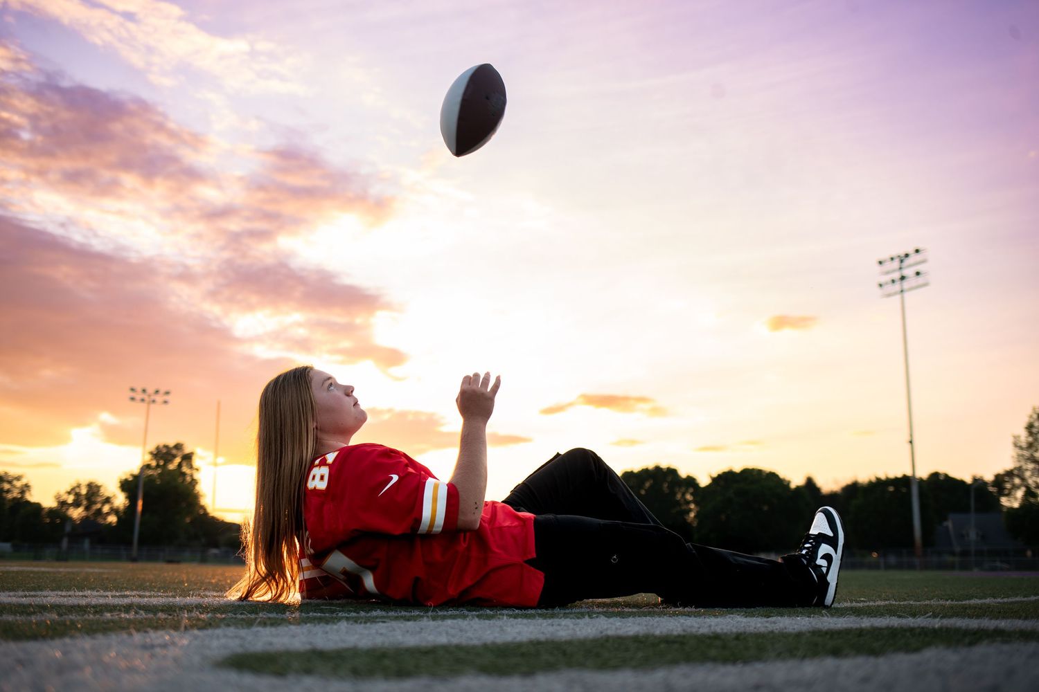 A football soars through the air during a sunset game with stadium lights glowing in the background.
