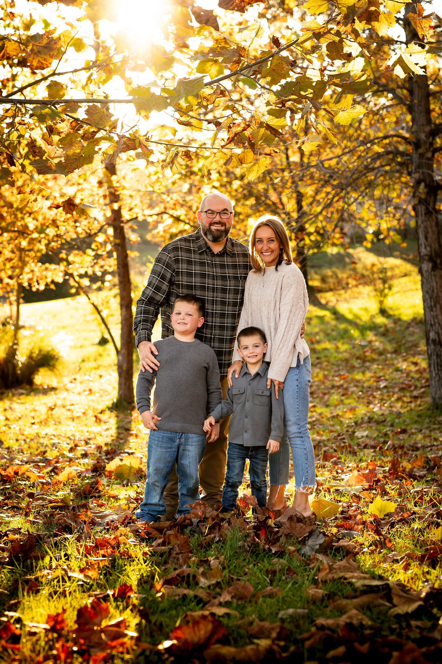A family stands together in a sunlit autumn forest surrounded by golden leaves and warm fall colors.