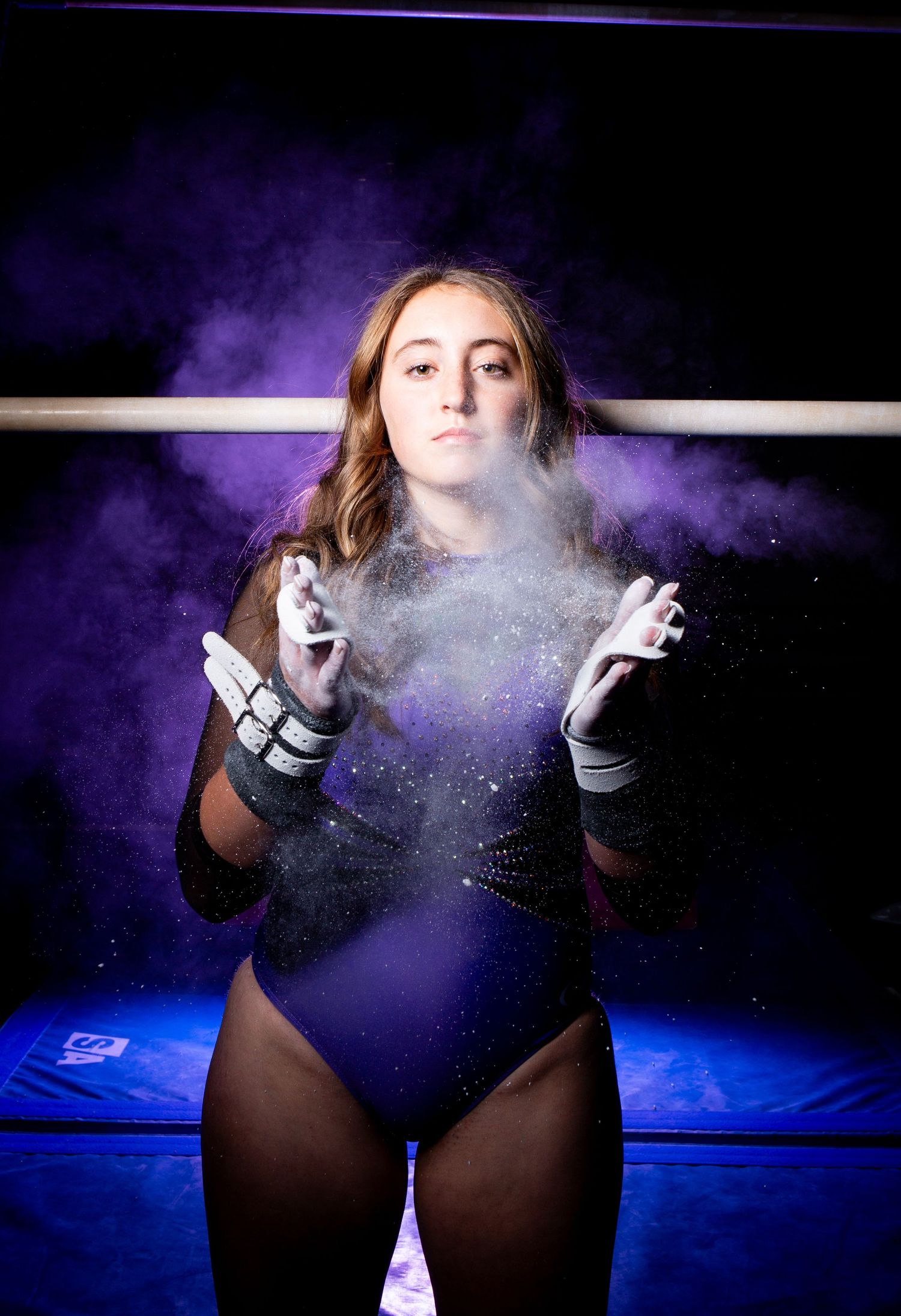 Artistic photo series showing gymnast clapping chalk powder creating dramatic purple-lit dust clouds in a dark setting.