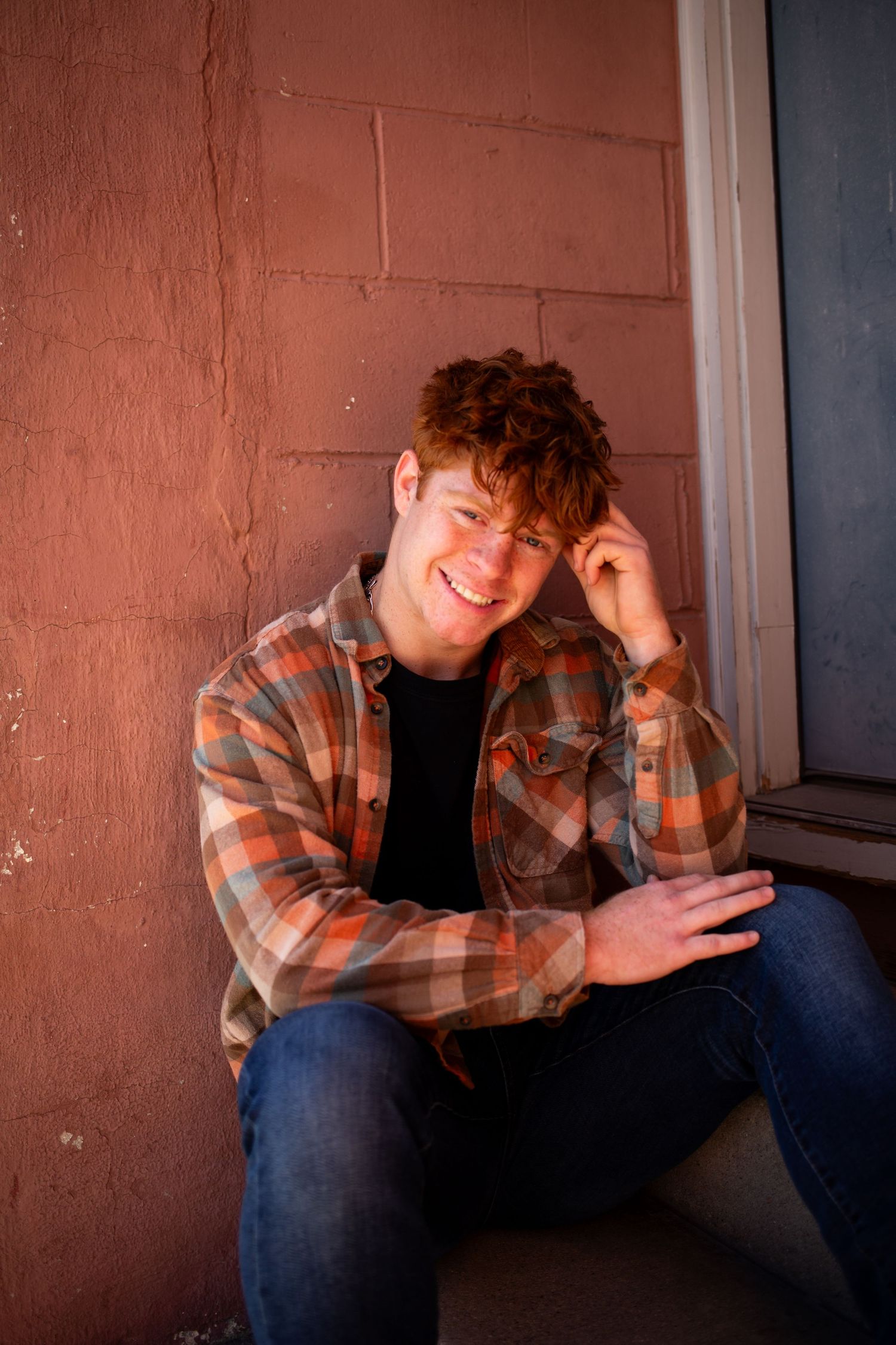 Person in plaid flannel shirt and jeans poses casually against brick wall in moody lighting sequence.