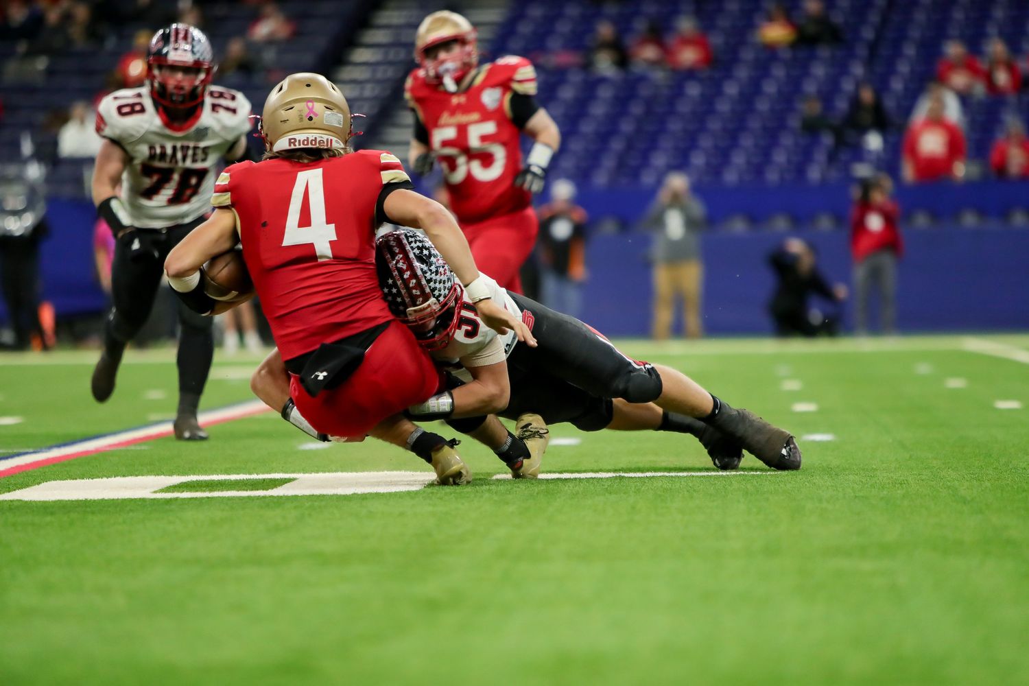 Football player in red jersey dives forward to make a tackle during a professional game at an indoor stadium.