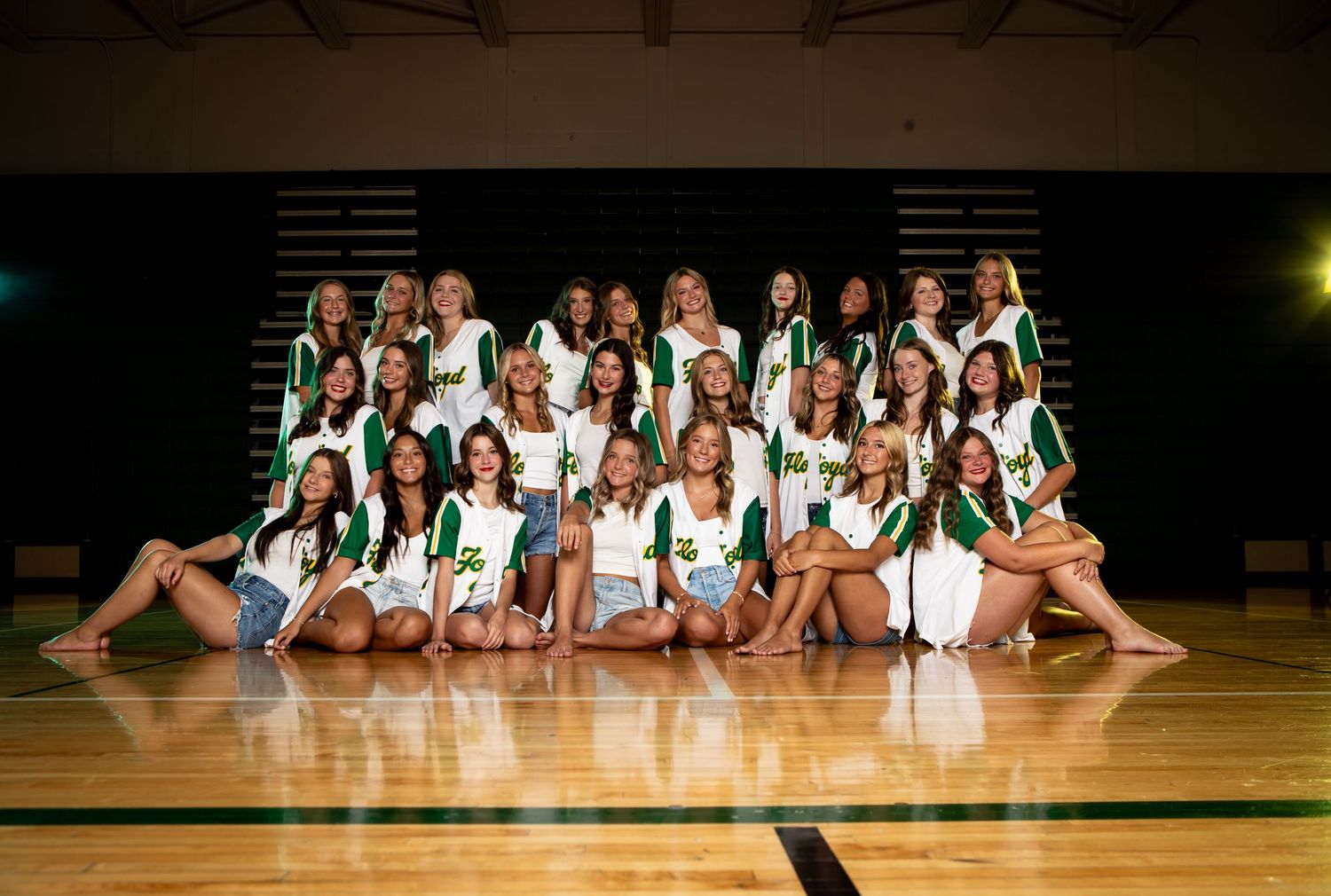 A cheerleading squad poses together on a gymnasium floor wearing green and white uniforms.
