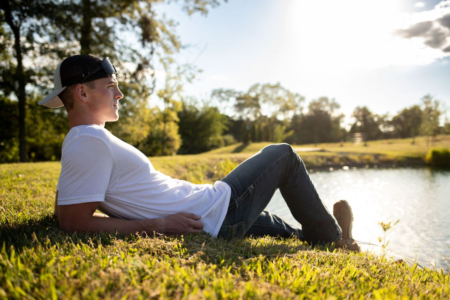Person relaxing on grassy hill by tranquil lake during golden sunset hour.