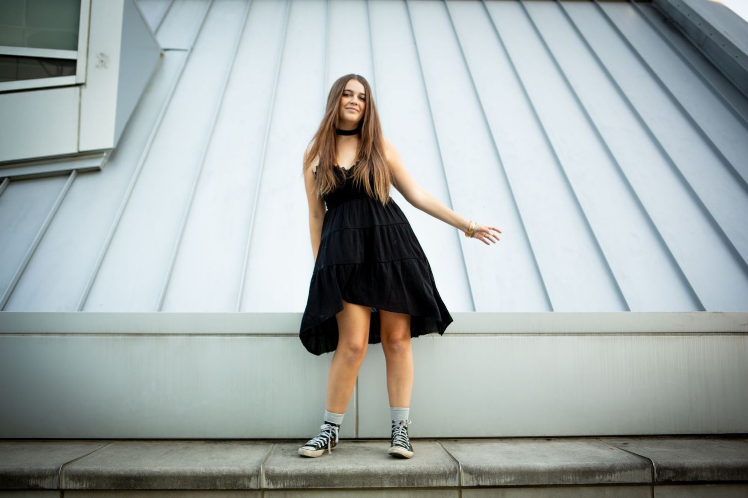 A person in a black dress performs dynamic dance movements on a white rooftop structure.