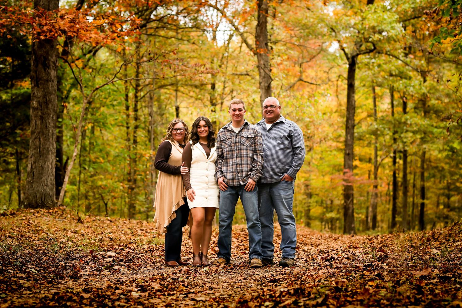 A group poses for autumn family portraits in a wooded area with vibrant fall foliage in the background.