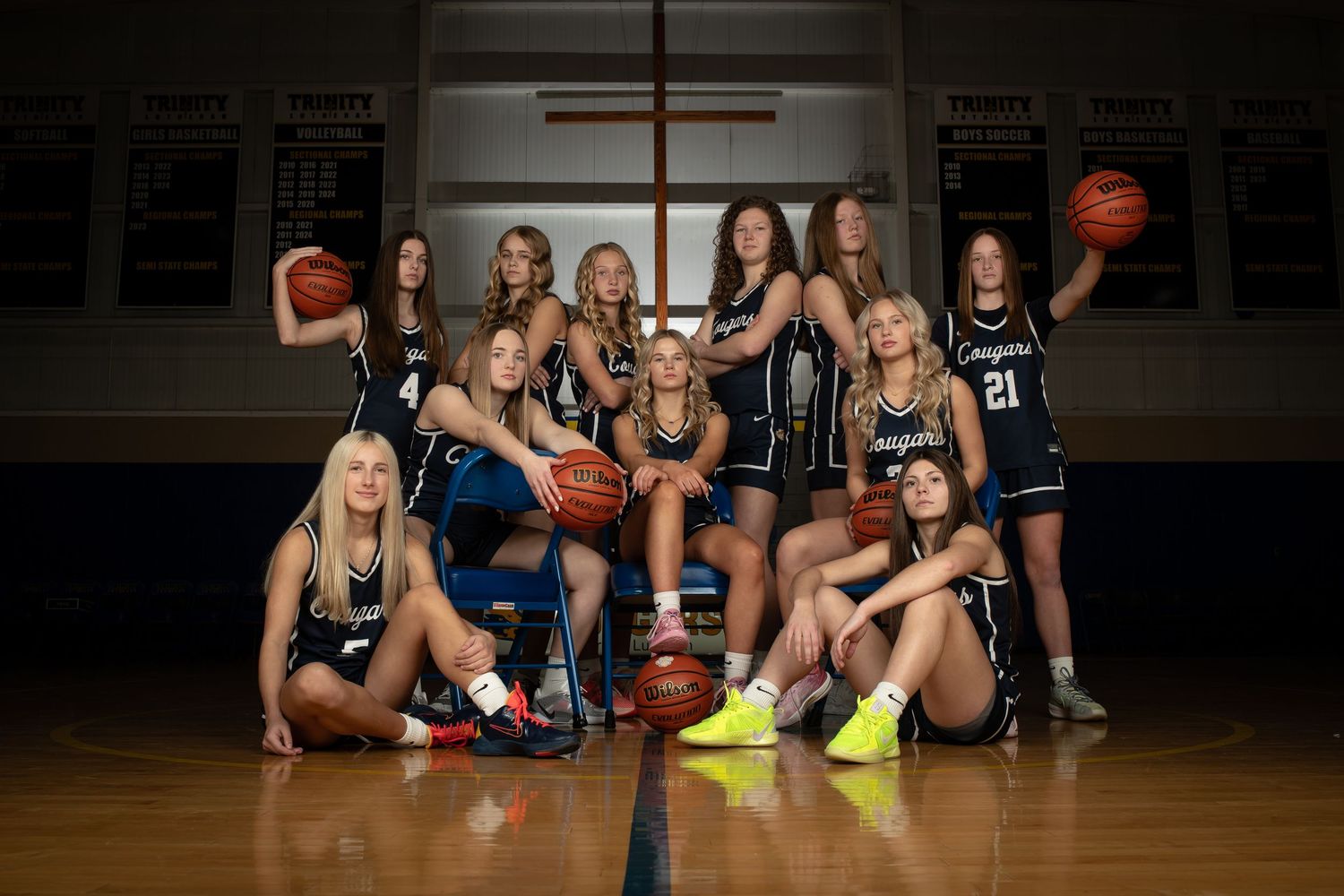 Basketball team poses for creative photo shoot on hardwood court with dramatic lighting and multiple poses.