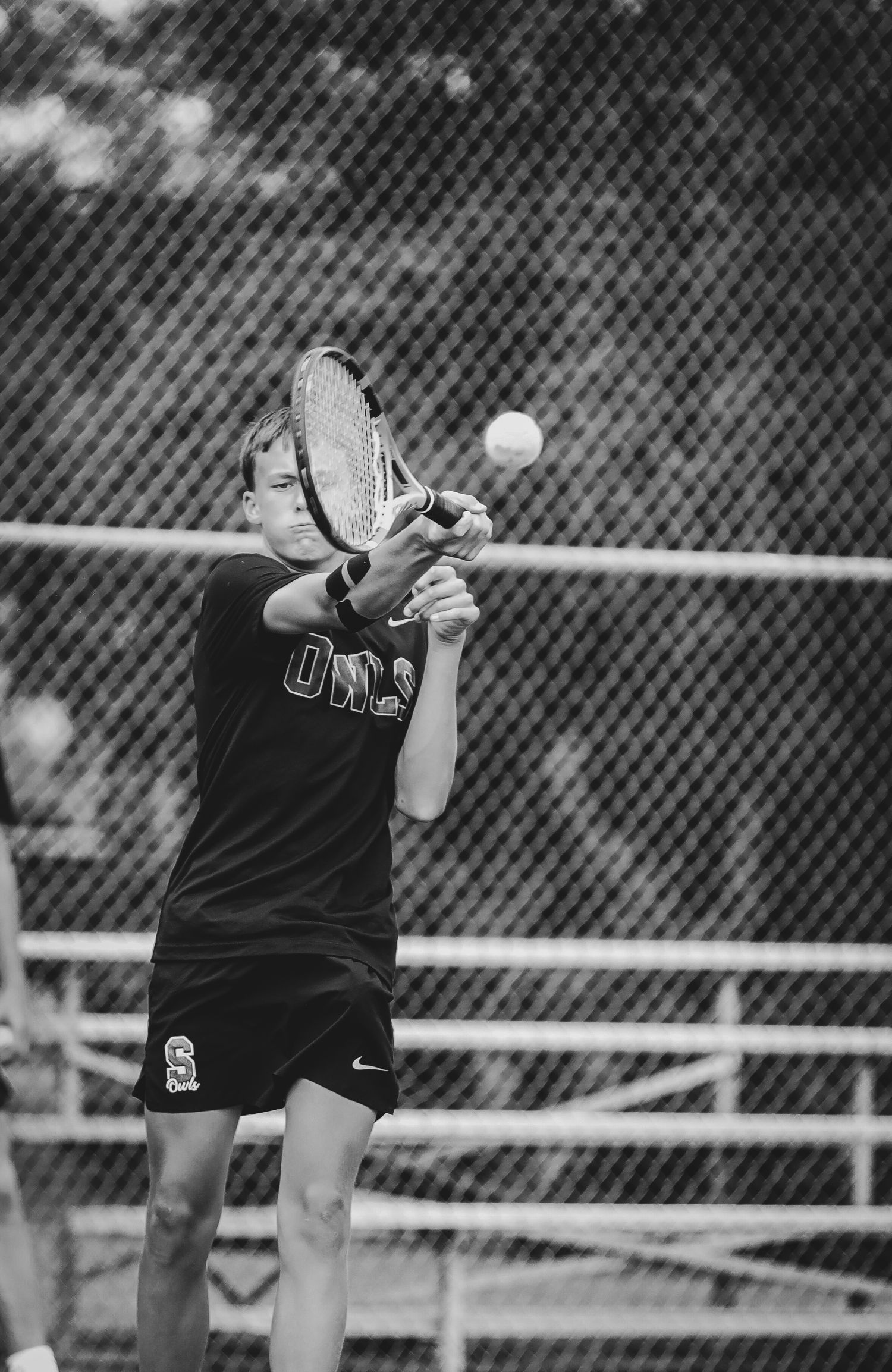 A black and white photo sequence showing a tennis player serving the ball over the net during a match.