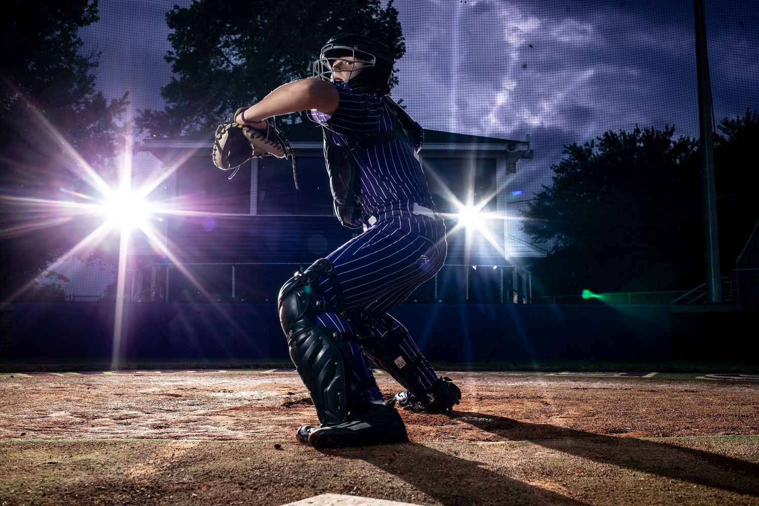 A baseball player prepares to throw a ball  at night with dramatic lighting effects and lens flares.
