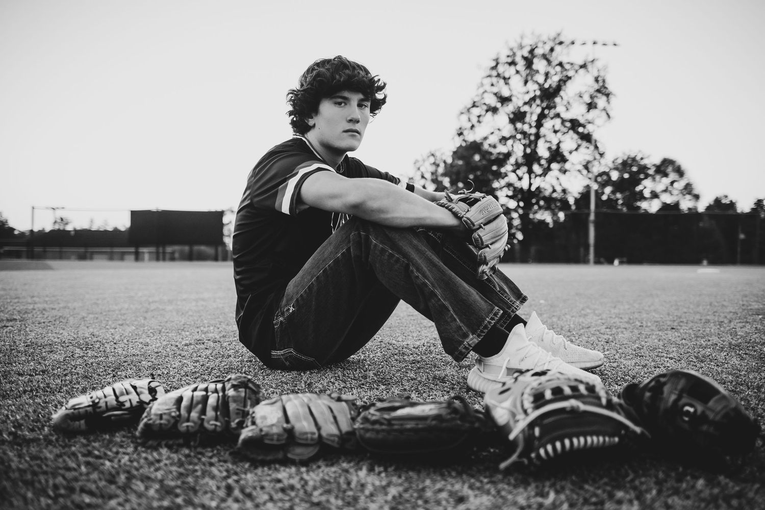 Black and white photo of a baseball player sitting on the field with baseball gloves and equipment laid out on the grass.