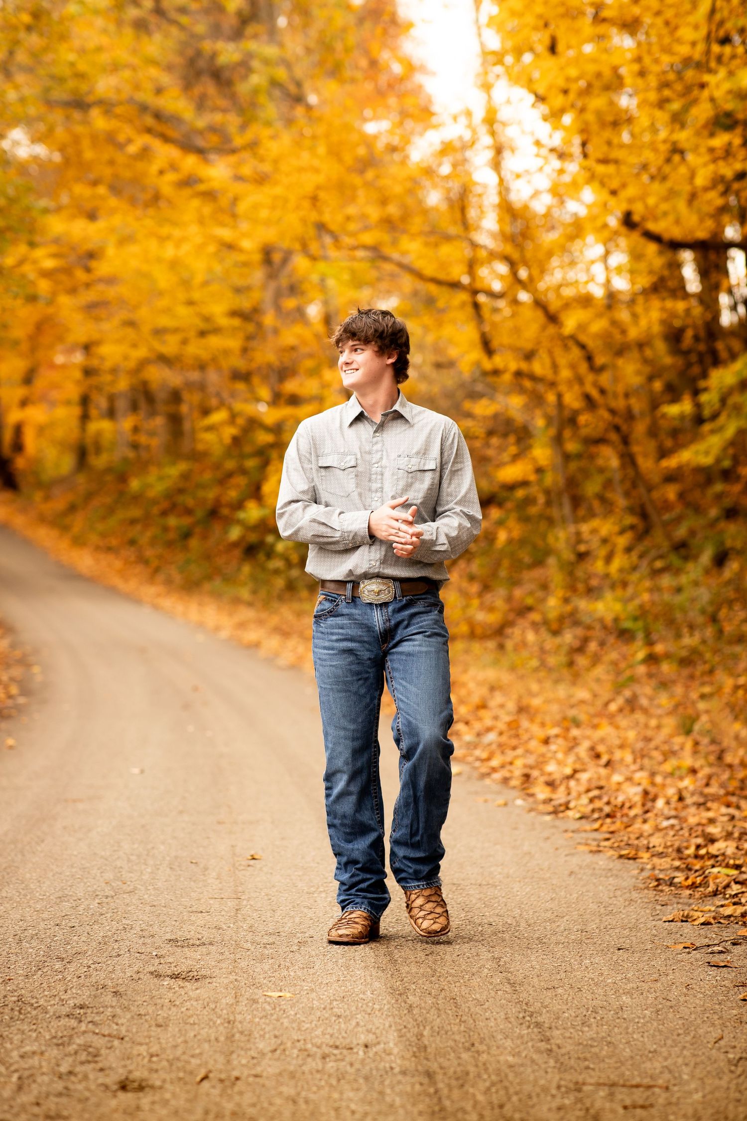 A person wearing jeans stands on a dirt path surrounded by vibrant golden autumn foliage and fallen leaves.