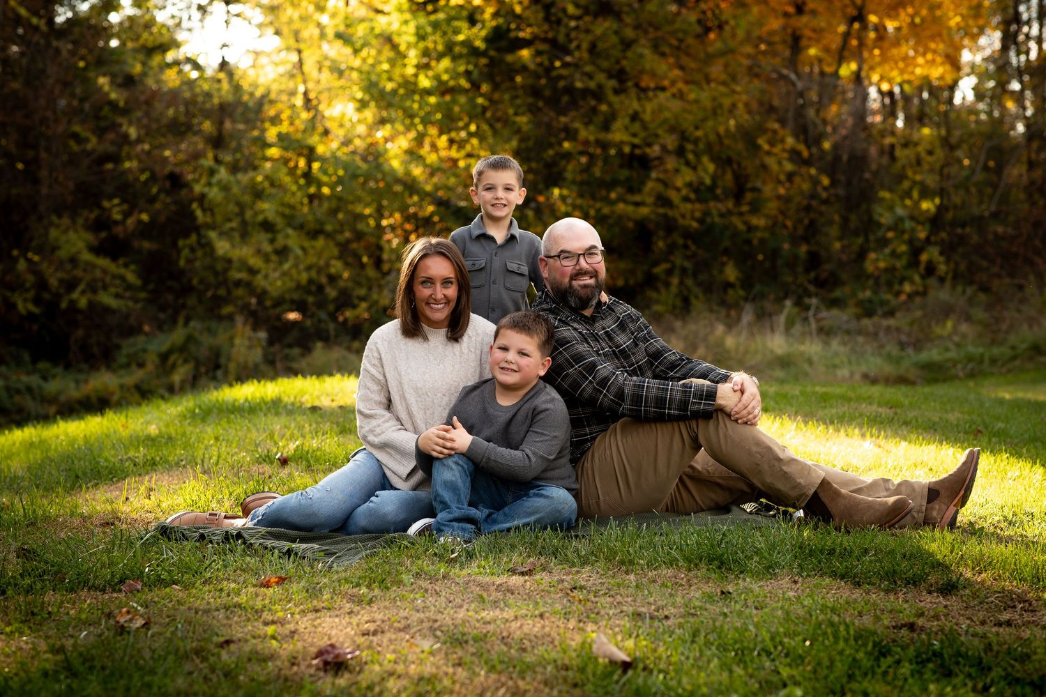 A family relaxes together on grass during a golden hour photoshoot in an autumn setting.