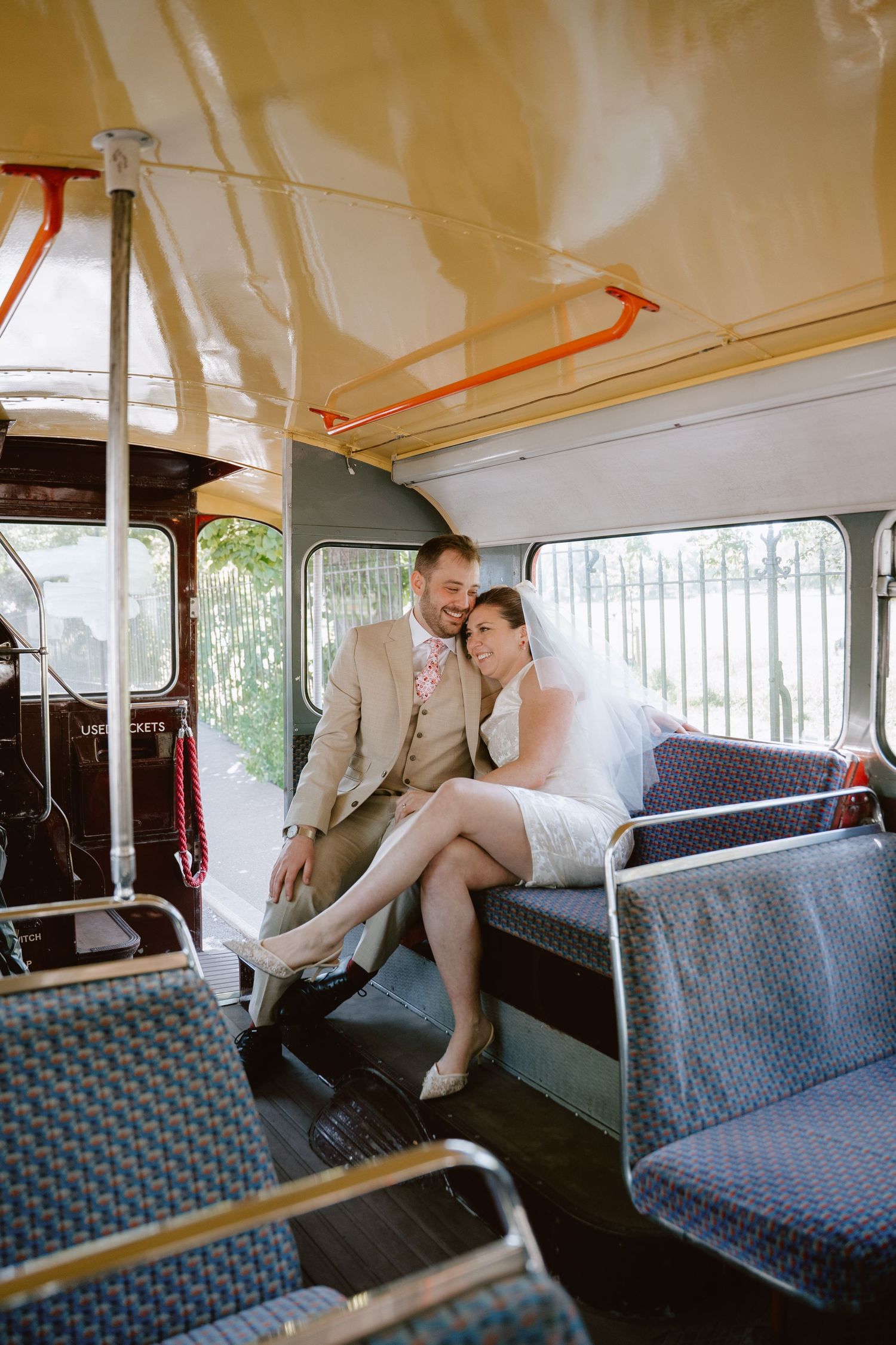 Bride and groom sitting together on a vintage bus, smiling, bride wearing a white dress and veil.