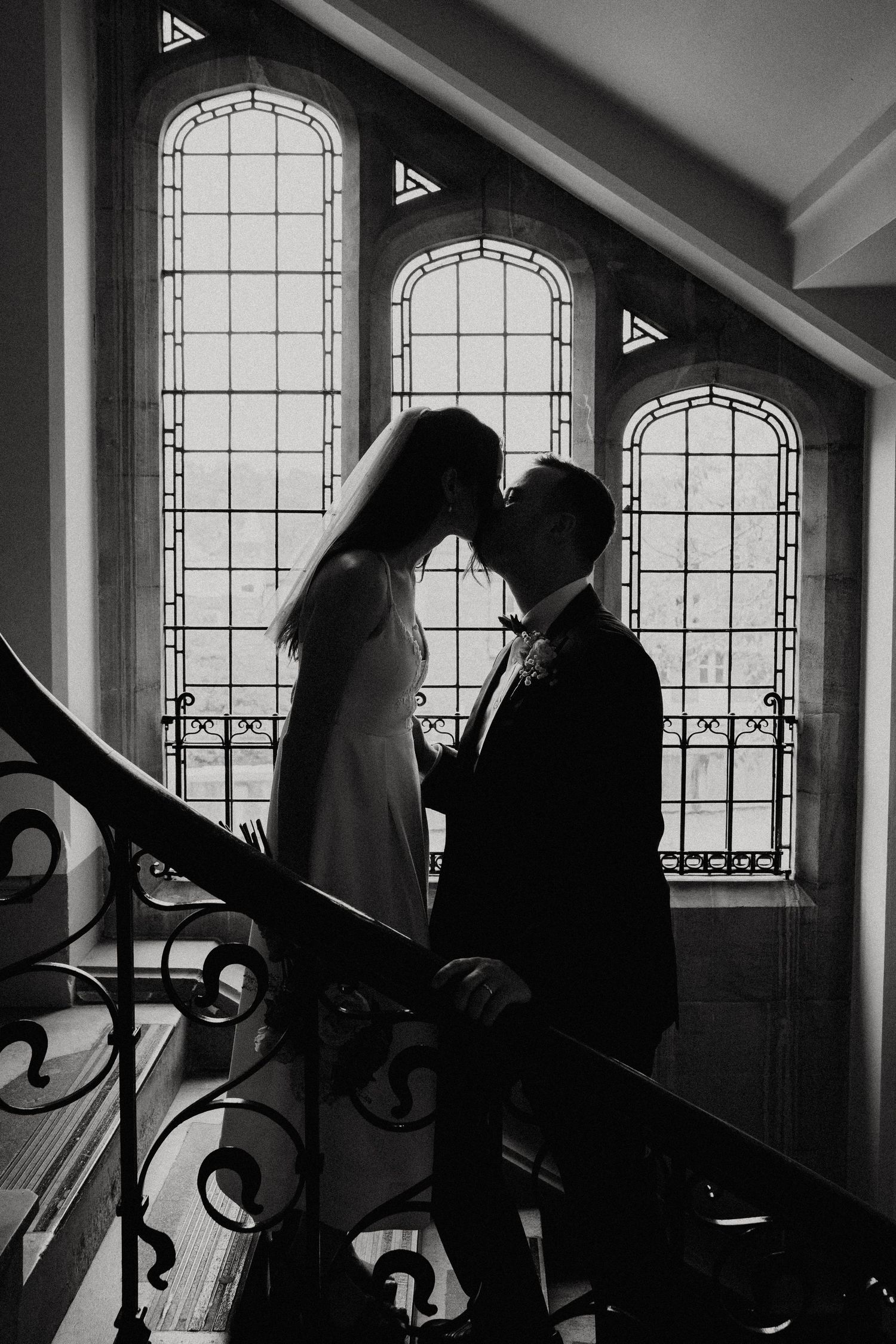 Black and white silhouettes walking past arched windows in a hallway.