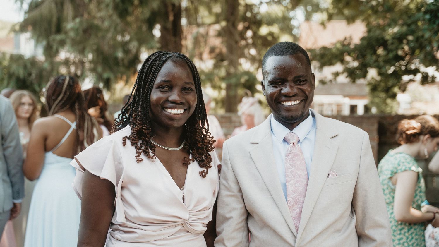 Wedding party members in formal attire stand together smiling during an outdoor celebration.