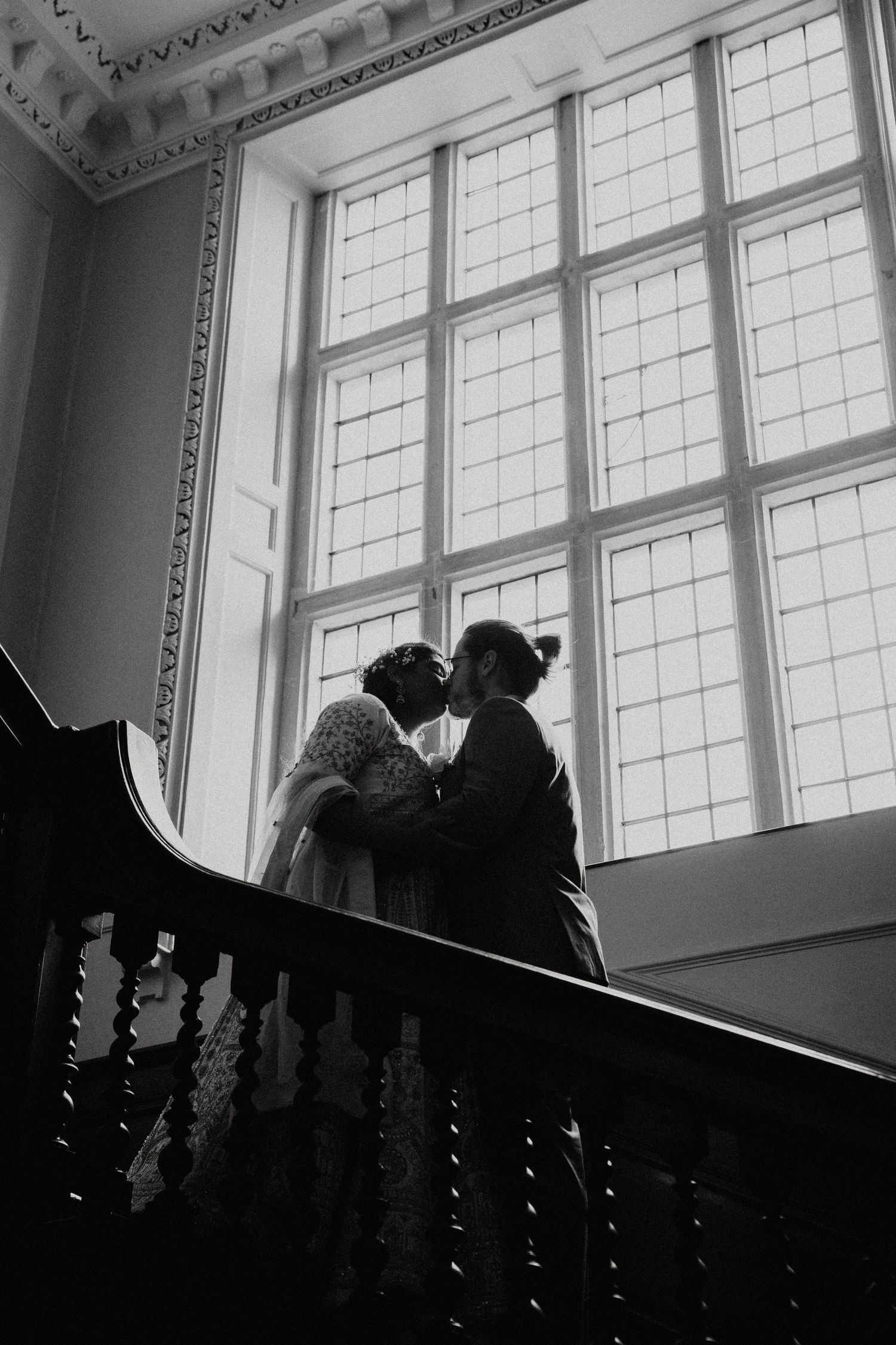 Dramatic black and white silhouettes of wedding party on grand staircase with ornate windows.