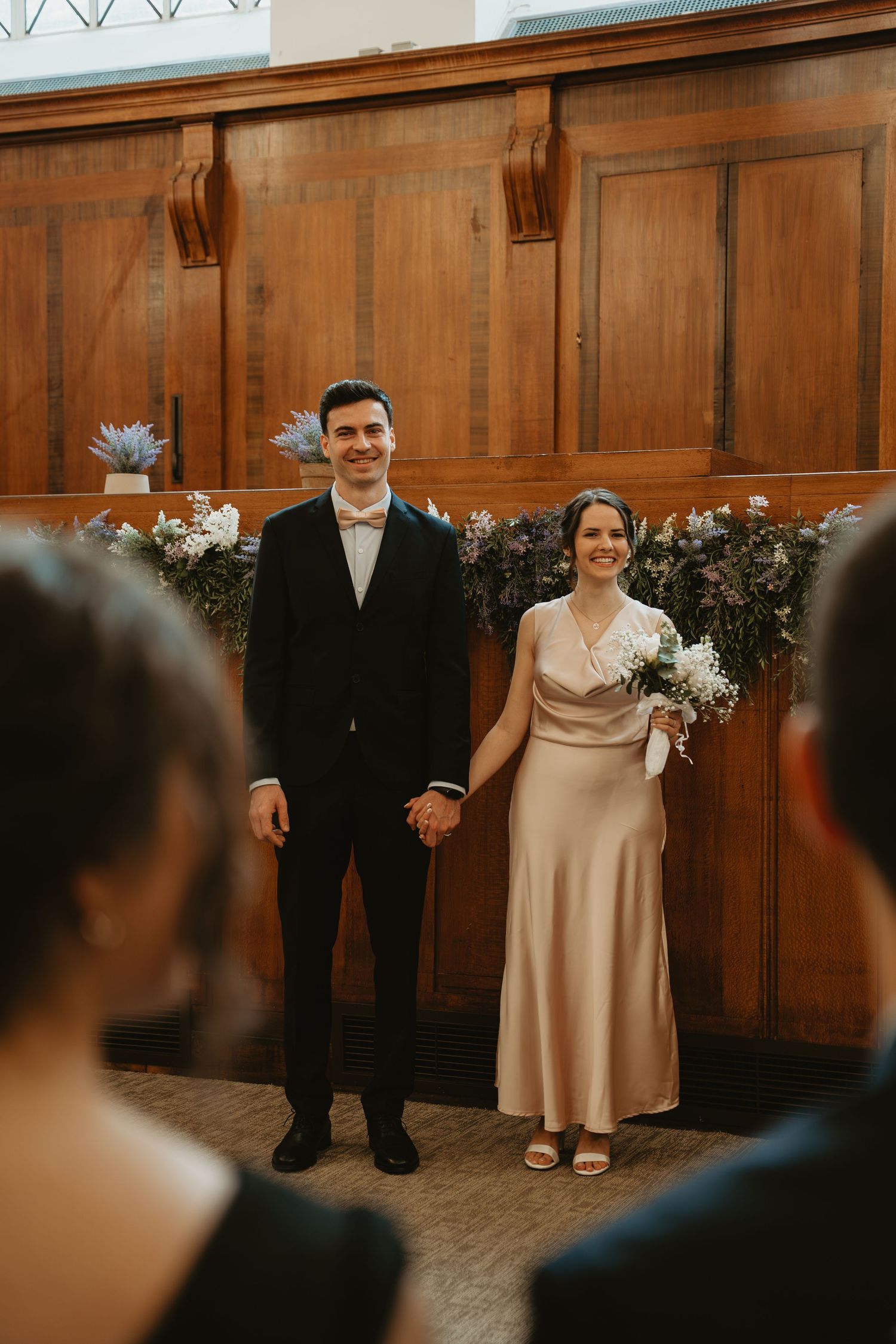 Wedding party members lined up against wood-paneled walls in formal attire.