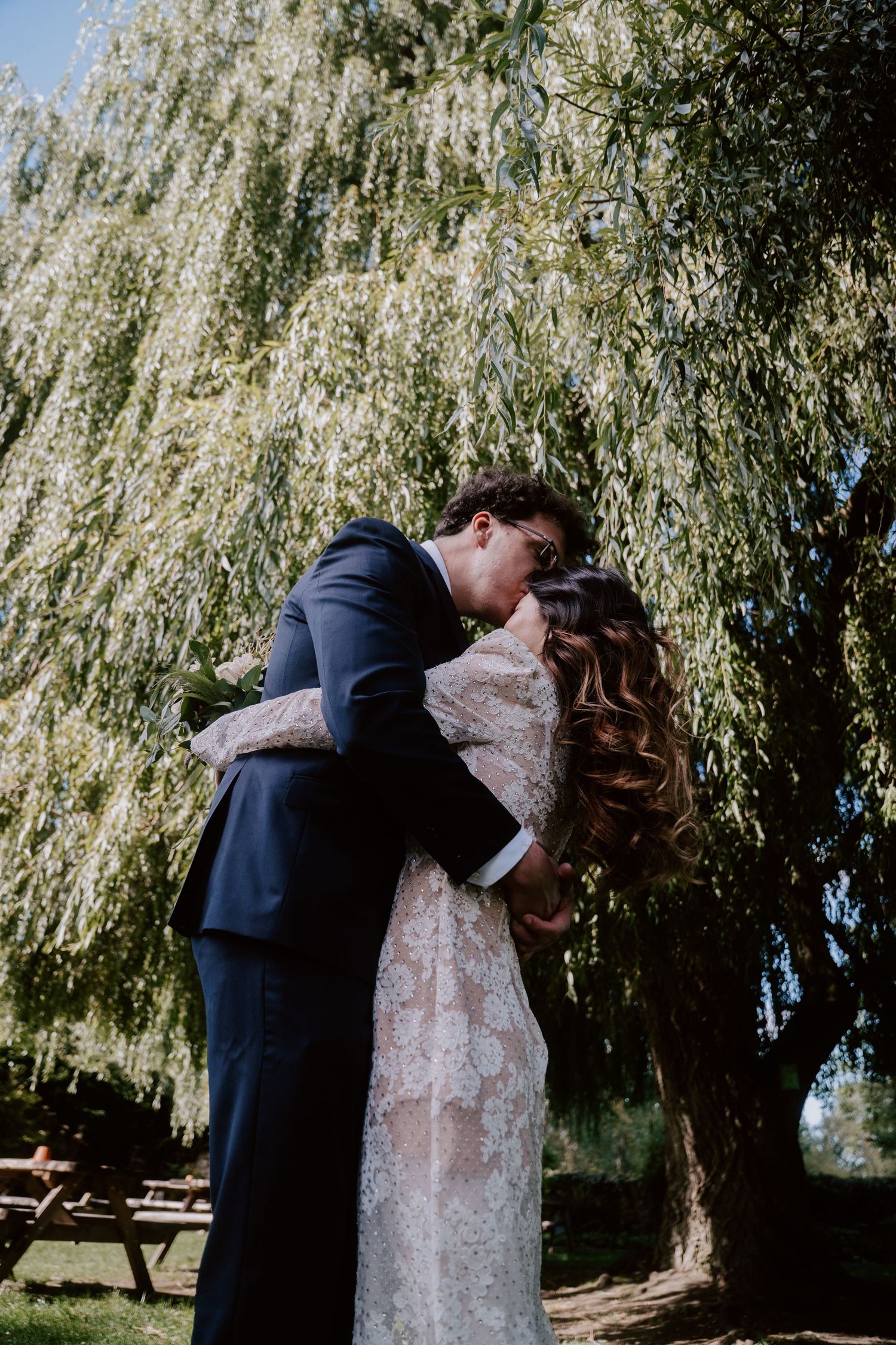 A romantic moment captured under a weeping willow tree on a wedding day.