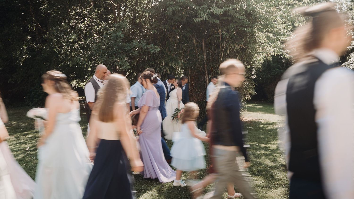Blurred motion shot of wedding guests mingling at an outdoor garden reception.