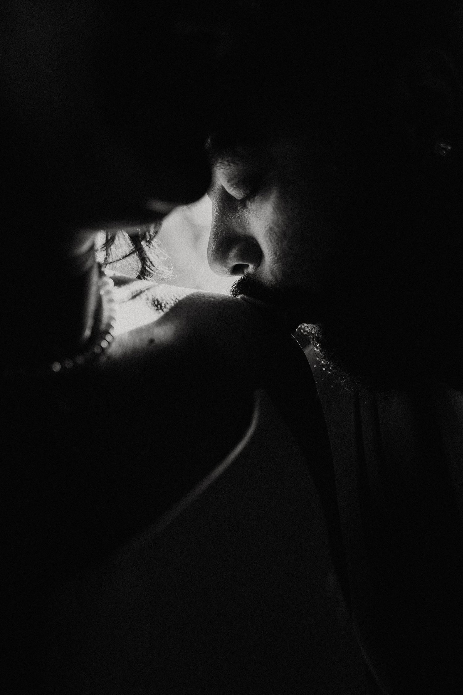 Black and white intimate portrait of a couple sharing a tender moment, with dramatic lighting highlighting their faces.