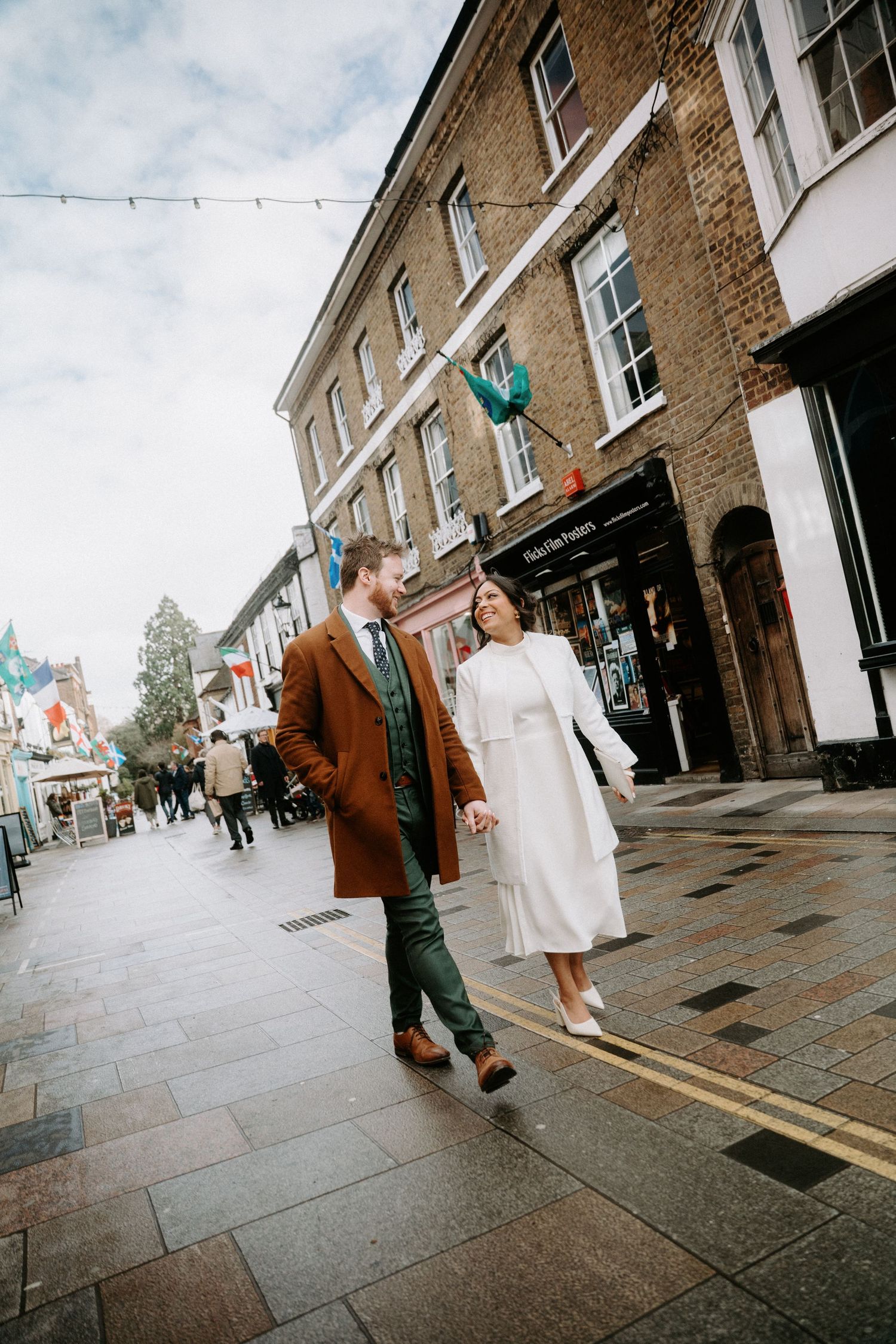 A couple walks along a charming brick-paved street in front of historic buildings on an overcast day.