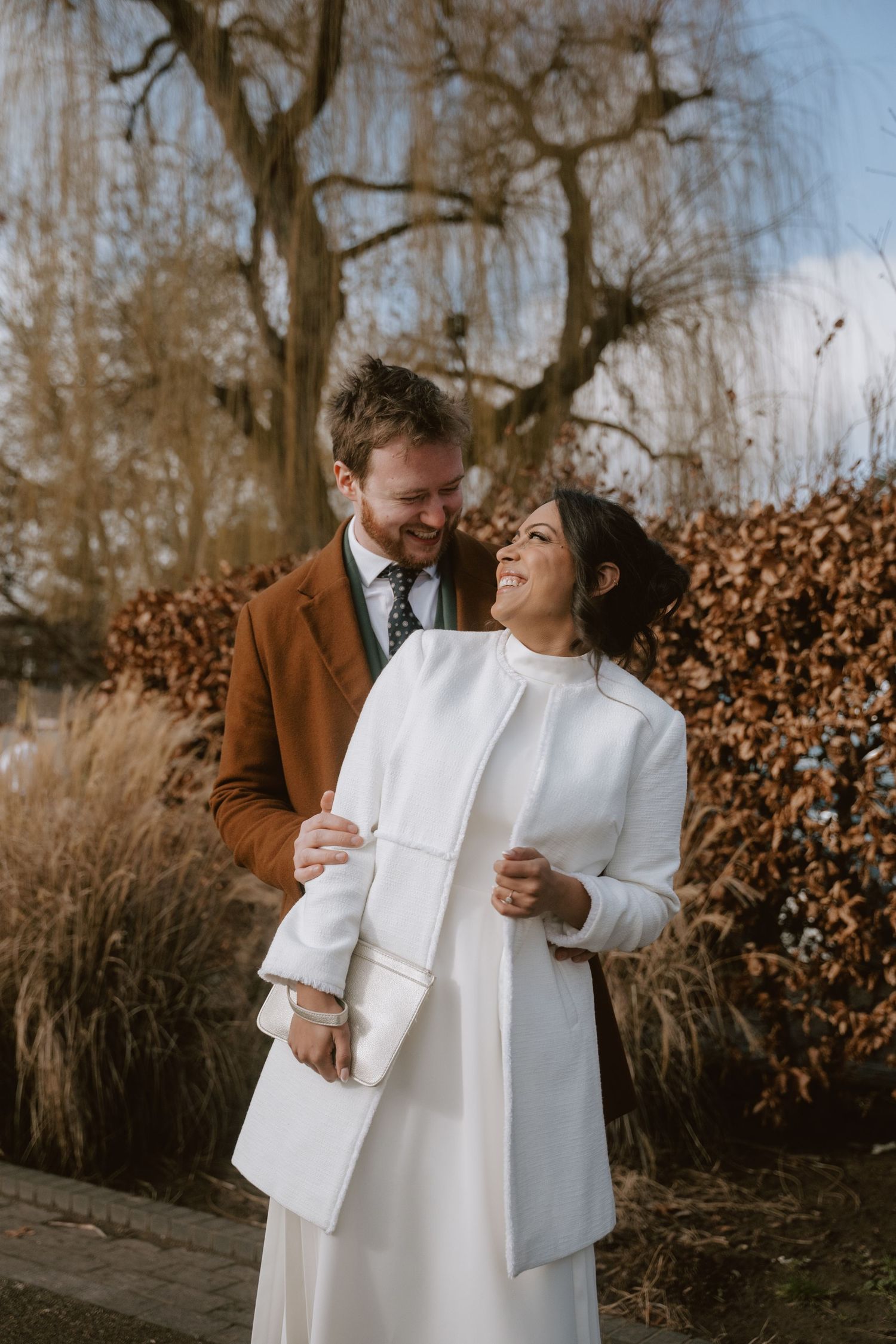 A couple shares tender moments in a fall garden setting wearing white and brown outfits against autumn foliage.