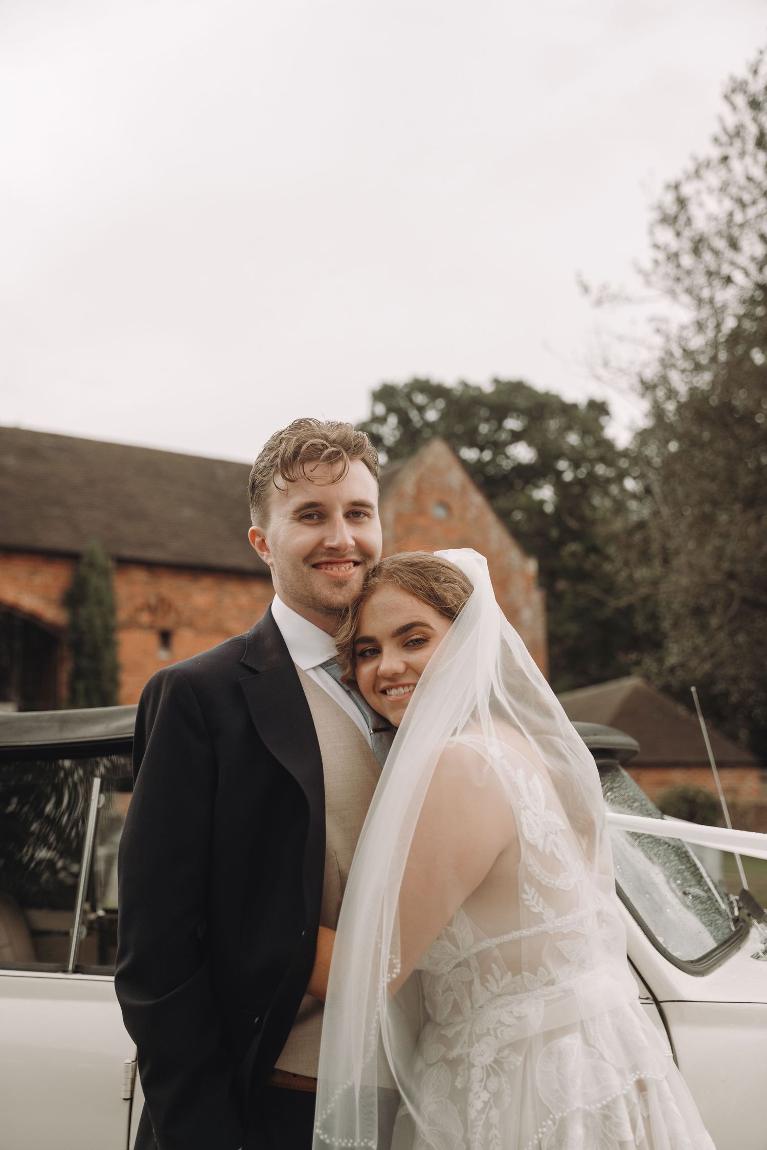 Newlyweds sharing a tender moment next to a classic white wedding car.