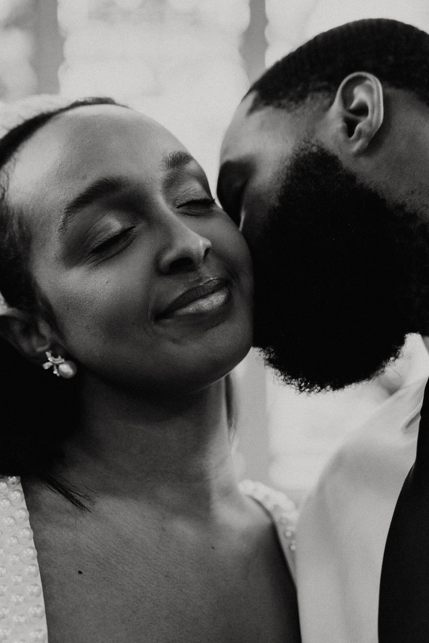 Black and white photo of a man tenderly kissing a smiling woman on the cheek, capturing a romantic moment.
