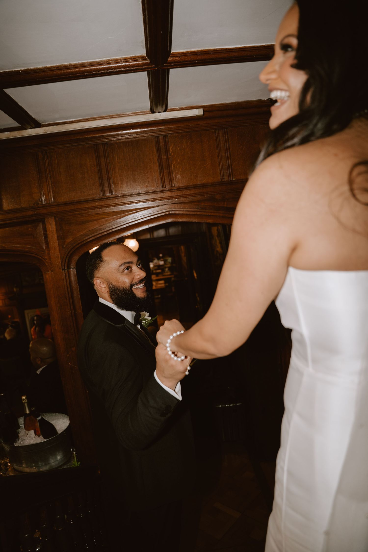 A joyful bride and groom share their first dance in an elegant wood-paneled venue, holding hands and smiling.